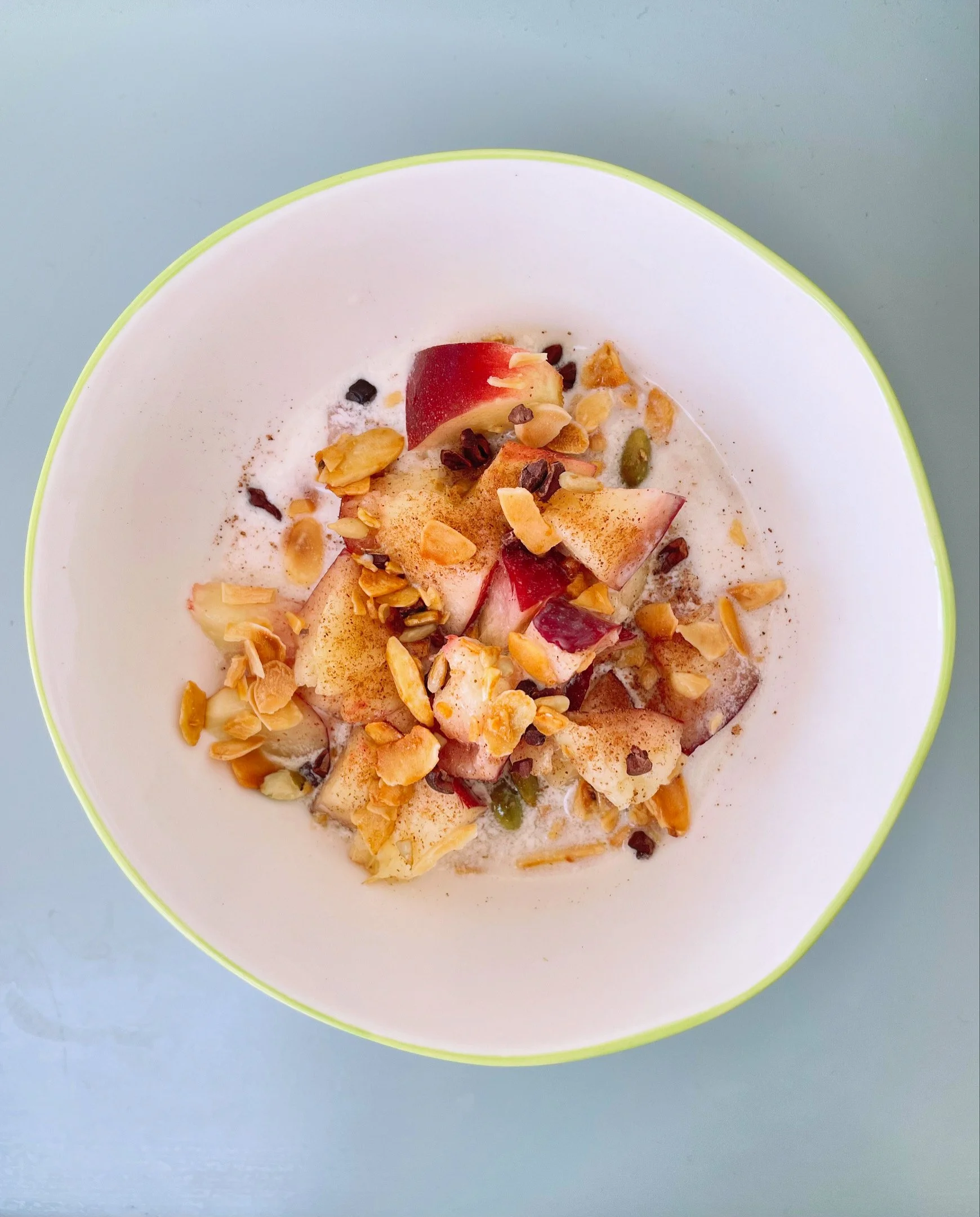 A bowl with sliced apples, chopped nuts, and cinnamon on top, placed on a light blue surface.