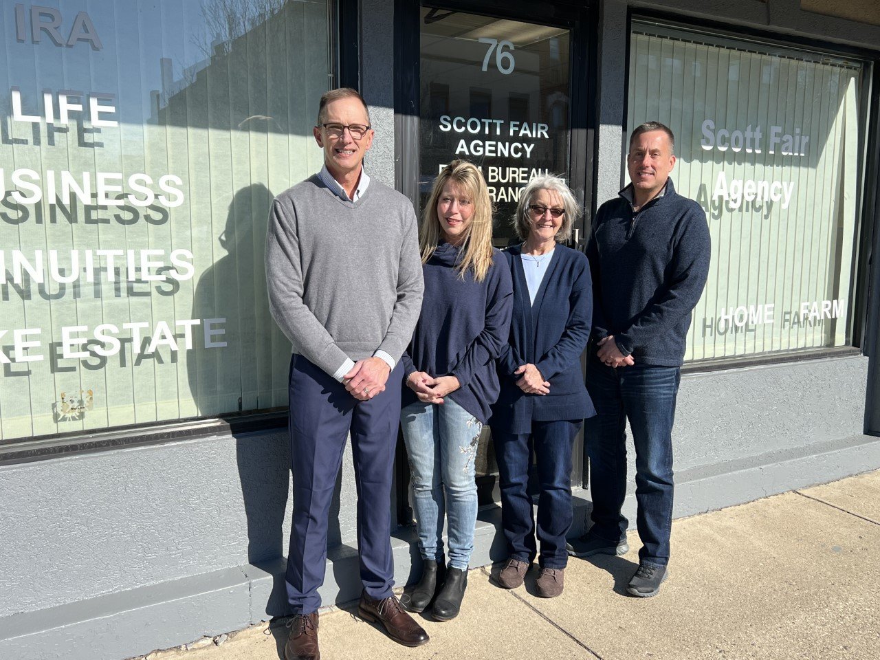Four people standing outside of a business window for Scott Fair Agency, posing for a photo in sunlight.