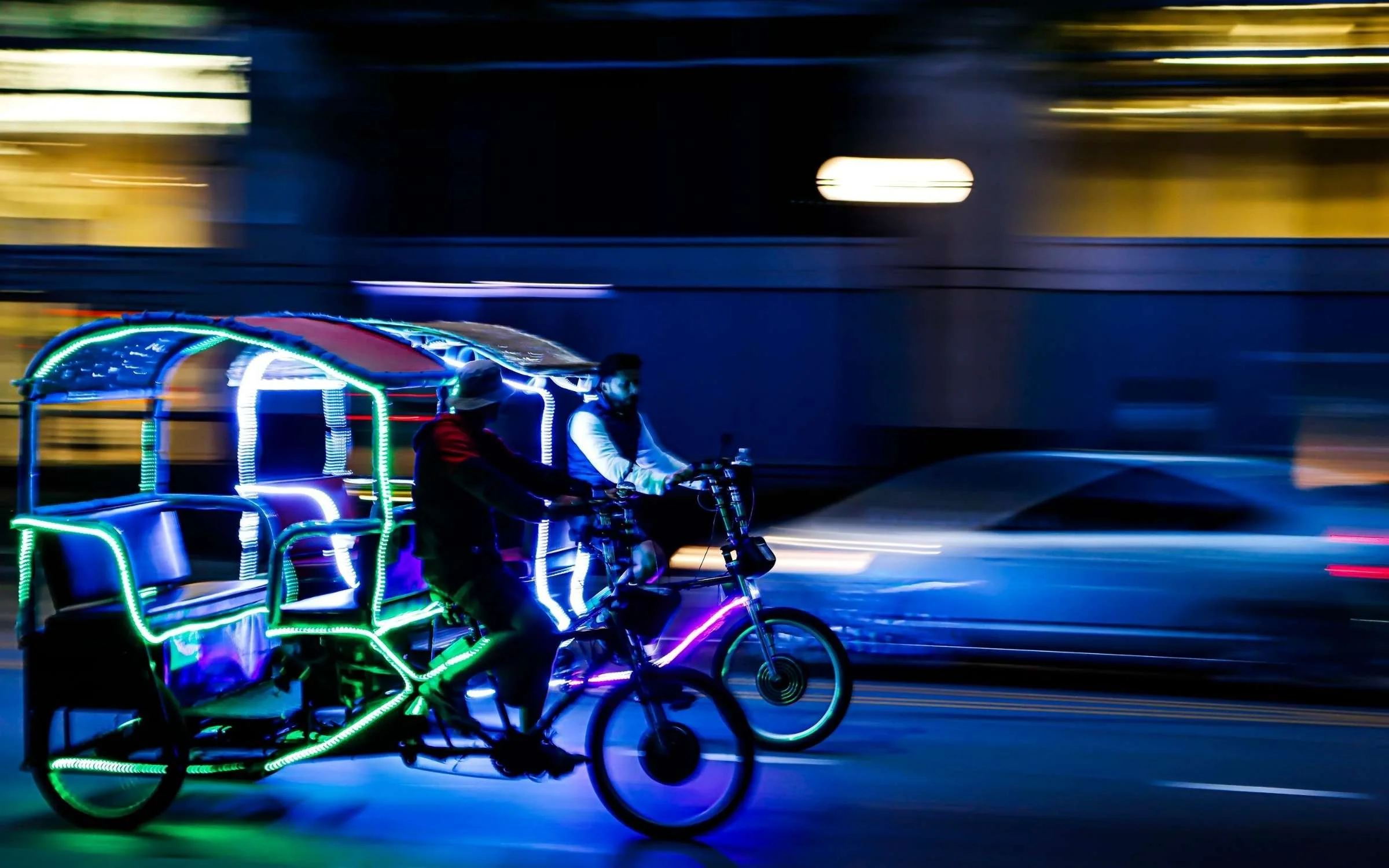 A bicycle rickshaw decorated with colorful neon lights in motion at night in Chicago, with blurred background.