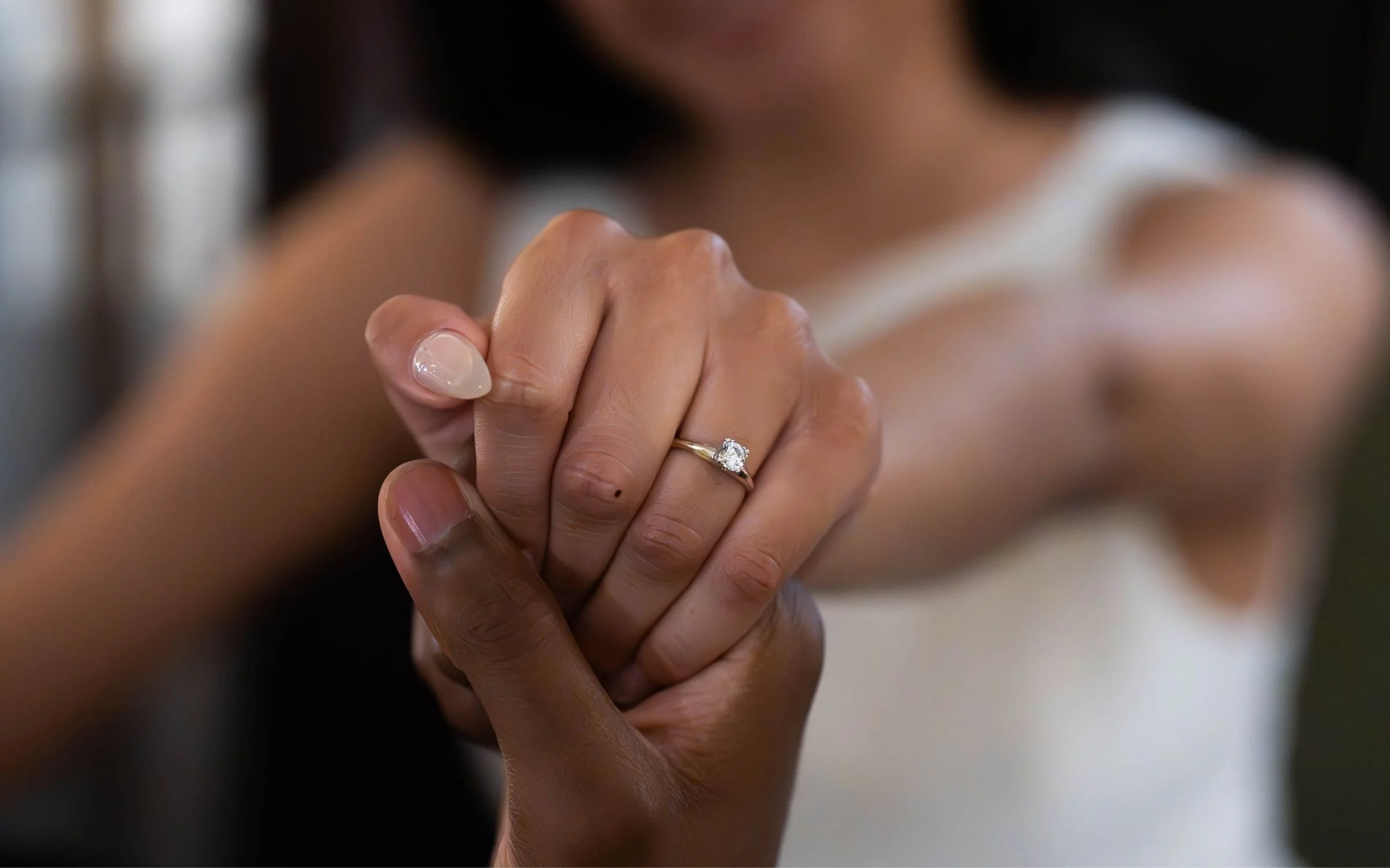 Close-up of a person holding hands, showing a diamond engagement ring on their finger.