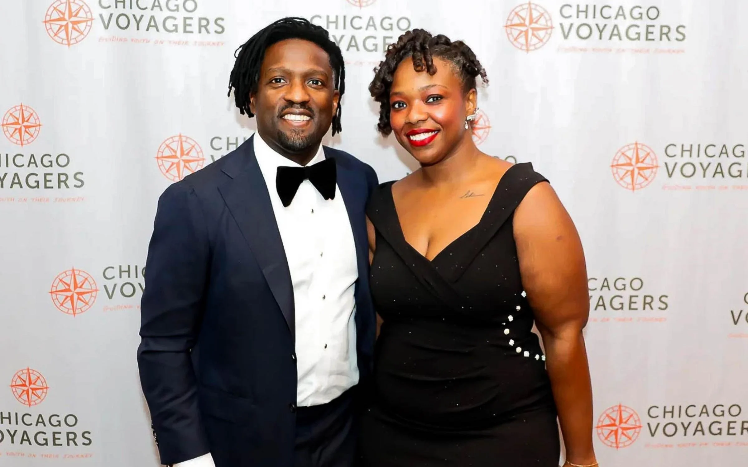A man and woman dressed in formal attire, smiling, standing in front of a backdrop with 'Chicago Voyagers' logos.