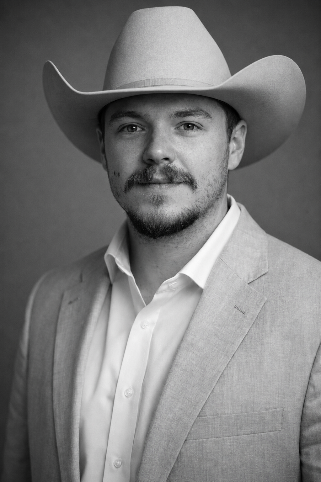Black and white portrait of a man wearing a cowboy hat, light-colored suit, and white shirt, looking at the camera with a slight smile, against a plain background.