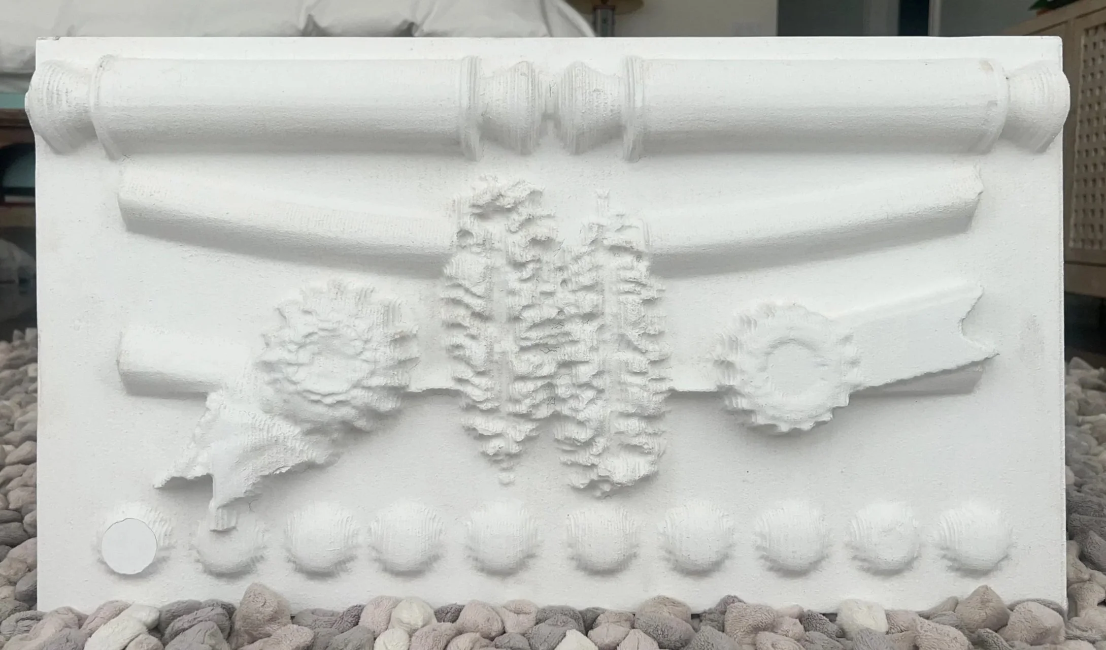White sculptural relief of a scroll, quill pen, and seal ribbons.
