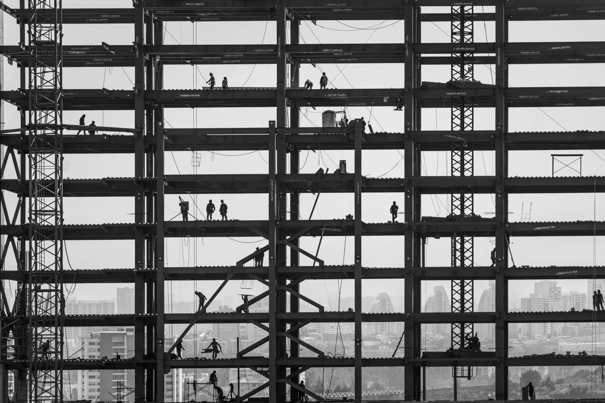 Estructura de un edificio en construcción con trabajadores en diferentes niveles, vista en blanco y negro.