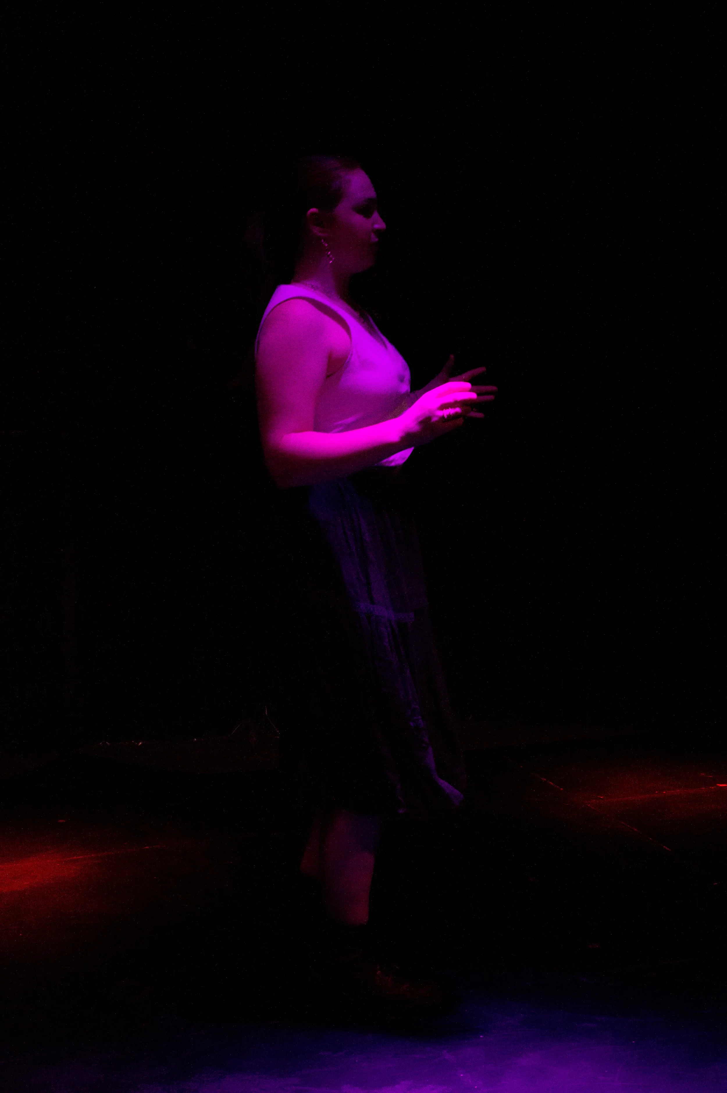 A woman is standing in a dark space with purple and red lighting, holding a phone with both hands, looking at the device.