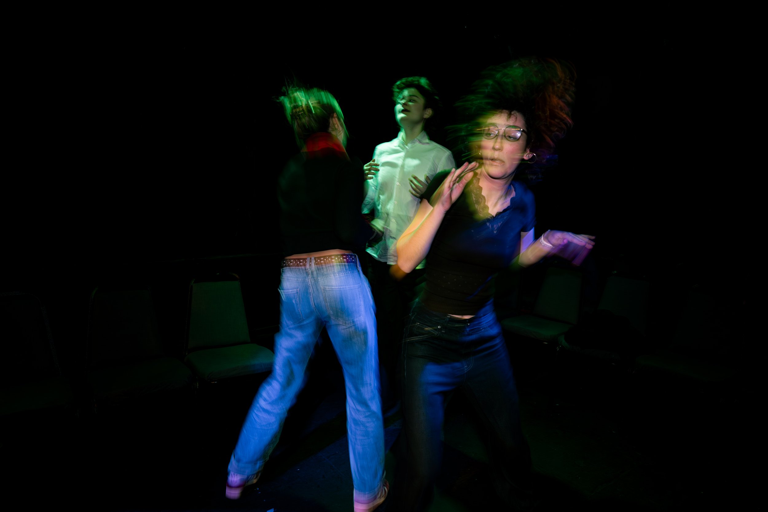 Three young women dancing in a dark room with colorful lights, appearing to be in motion and enjoying themselves.