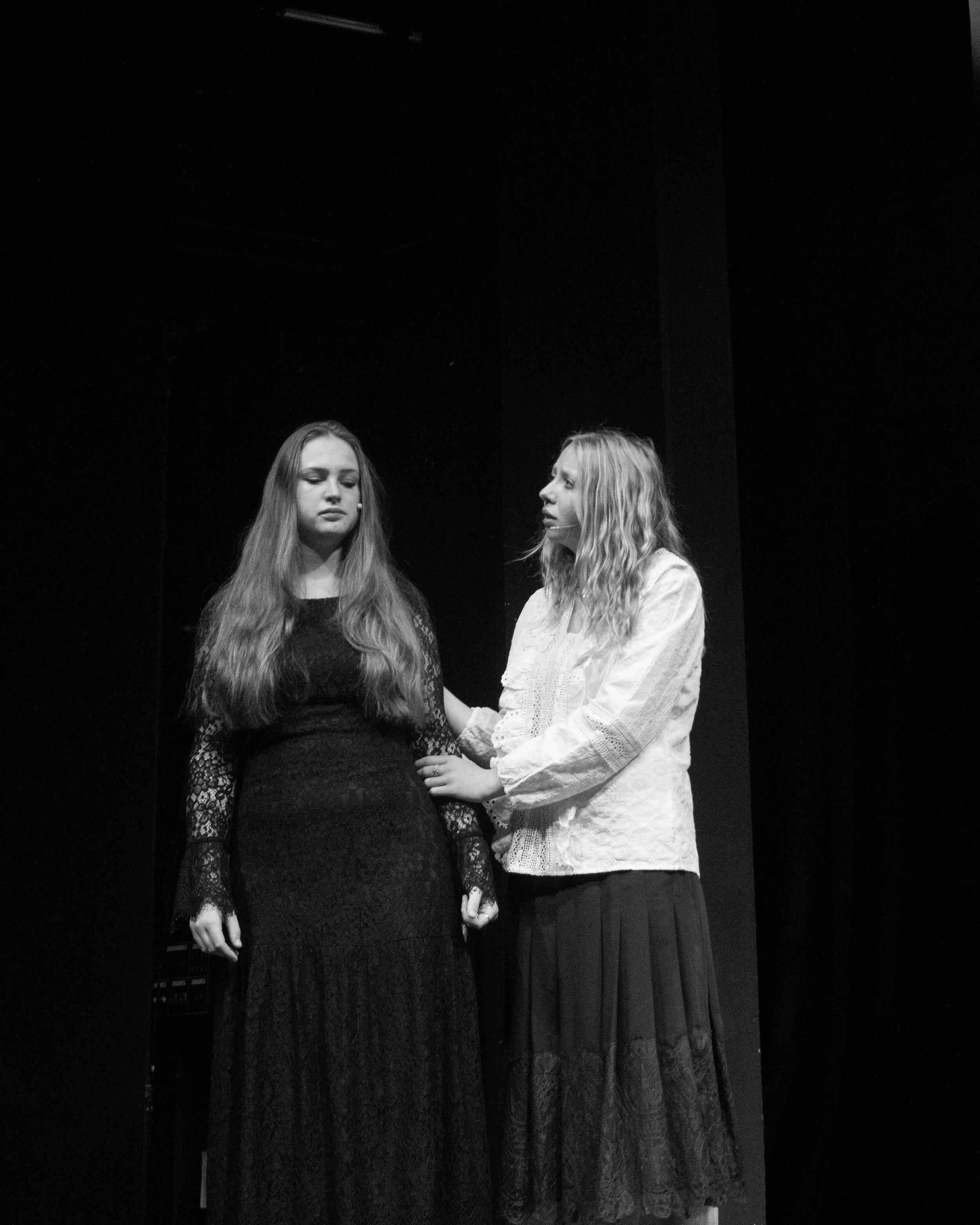 Two women standing close together, holding hands, on a stage with a dark background.