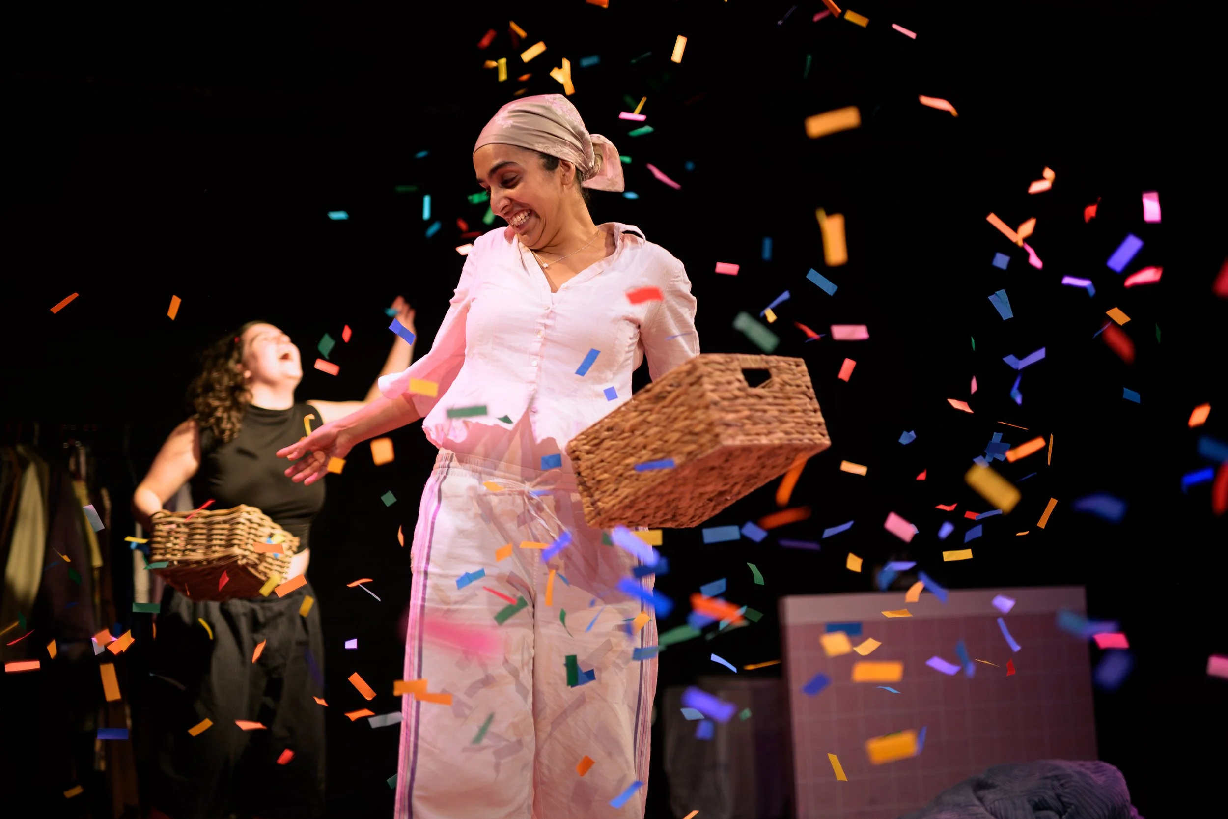 Woman smiling with headscarf, surrounded by colorful confetti, holding a basket, in a lively celebration.