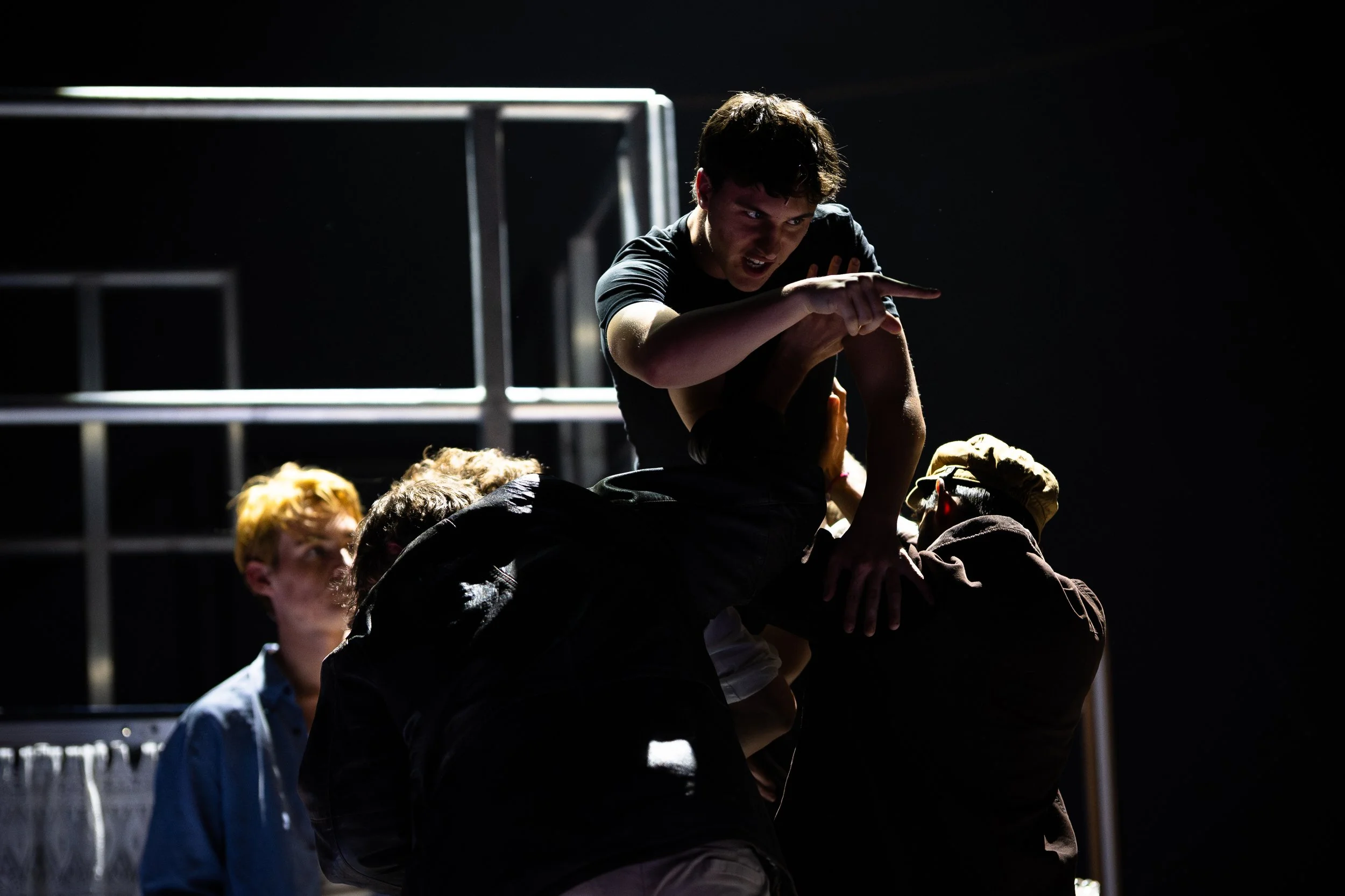 A dark scene with multiple people forming a human pyramid in a dimly lit environment.