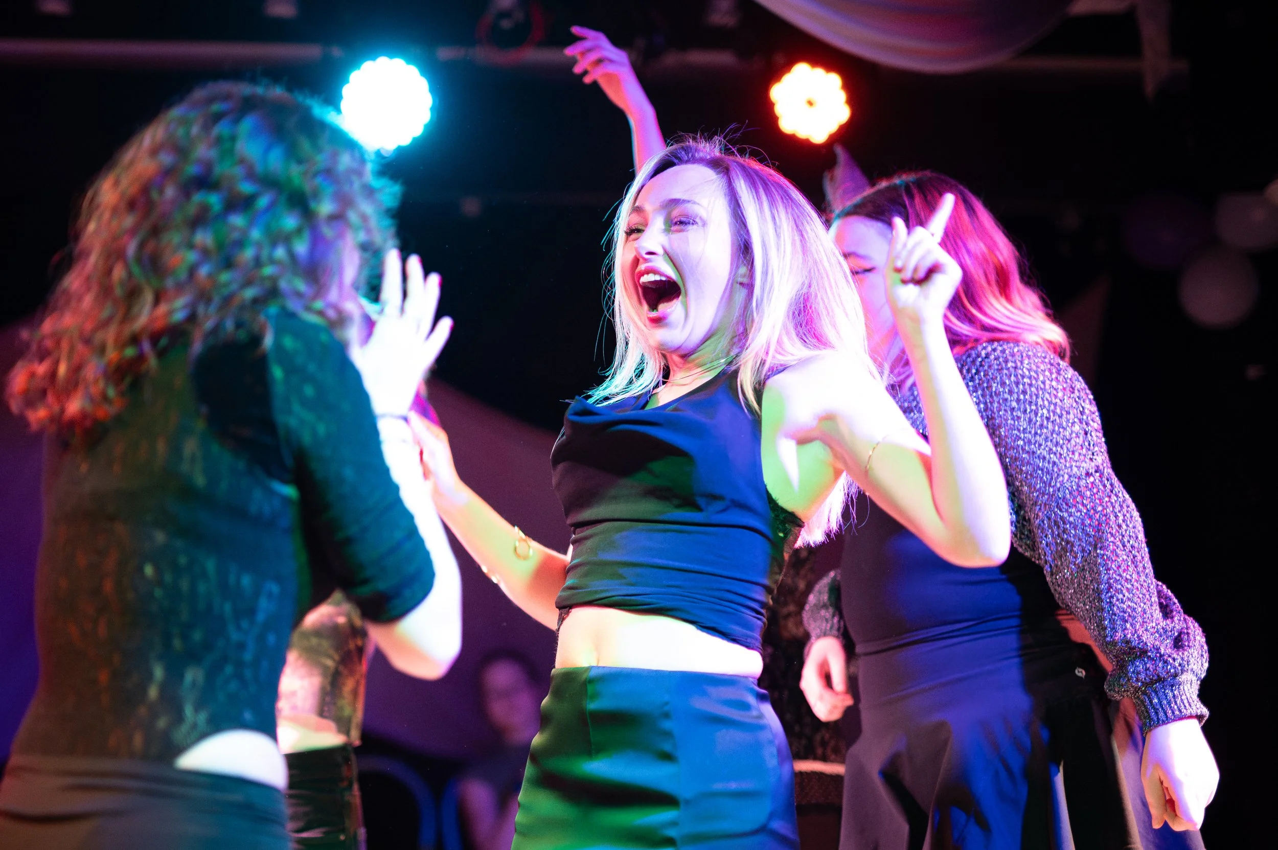 Women dancing and socializing at a lively party or club with colorful lighting.