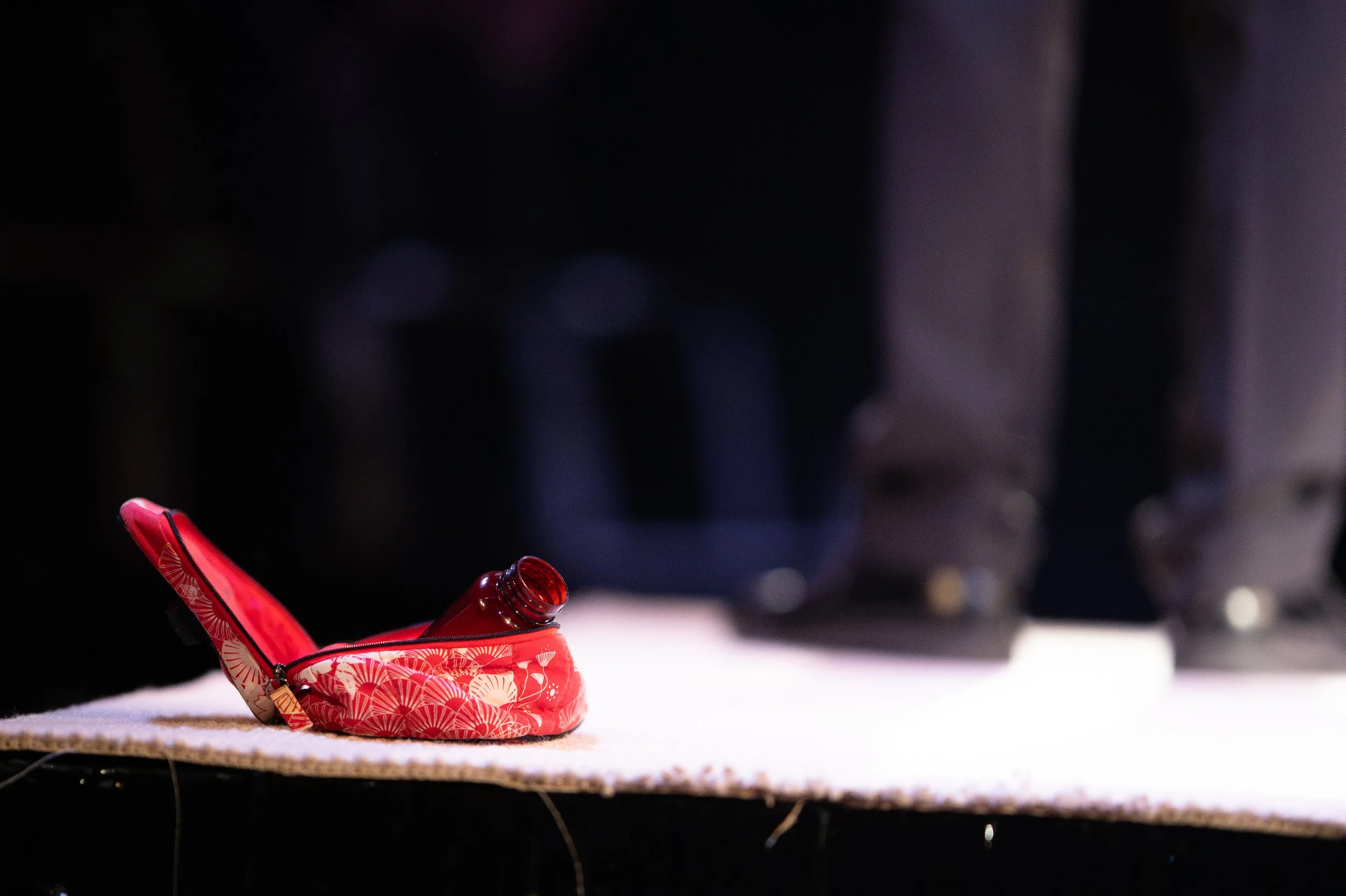 An emptied red potion bottle and a red pouch with a floral pattern sit on the floor, with a blurred background.