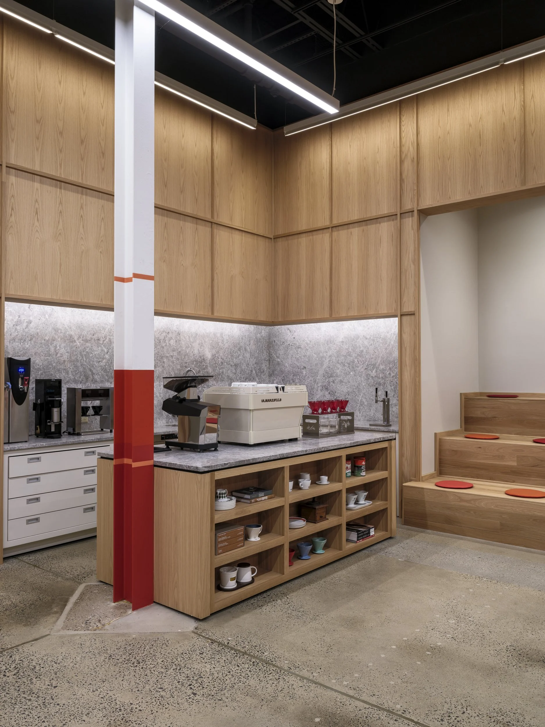 Coffee station with coffee equipment, cups, and a built-in seating area with cushions in a modern interior.