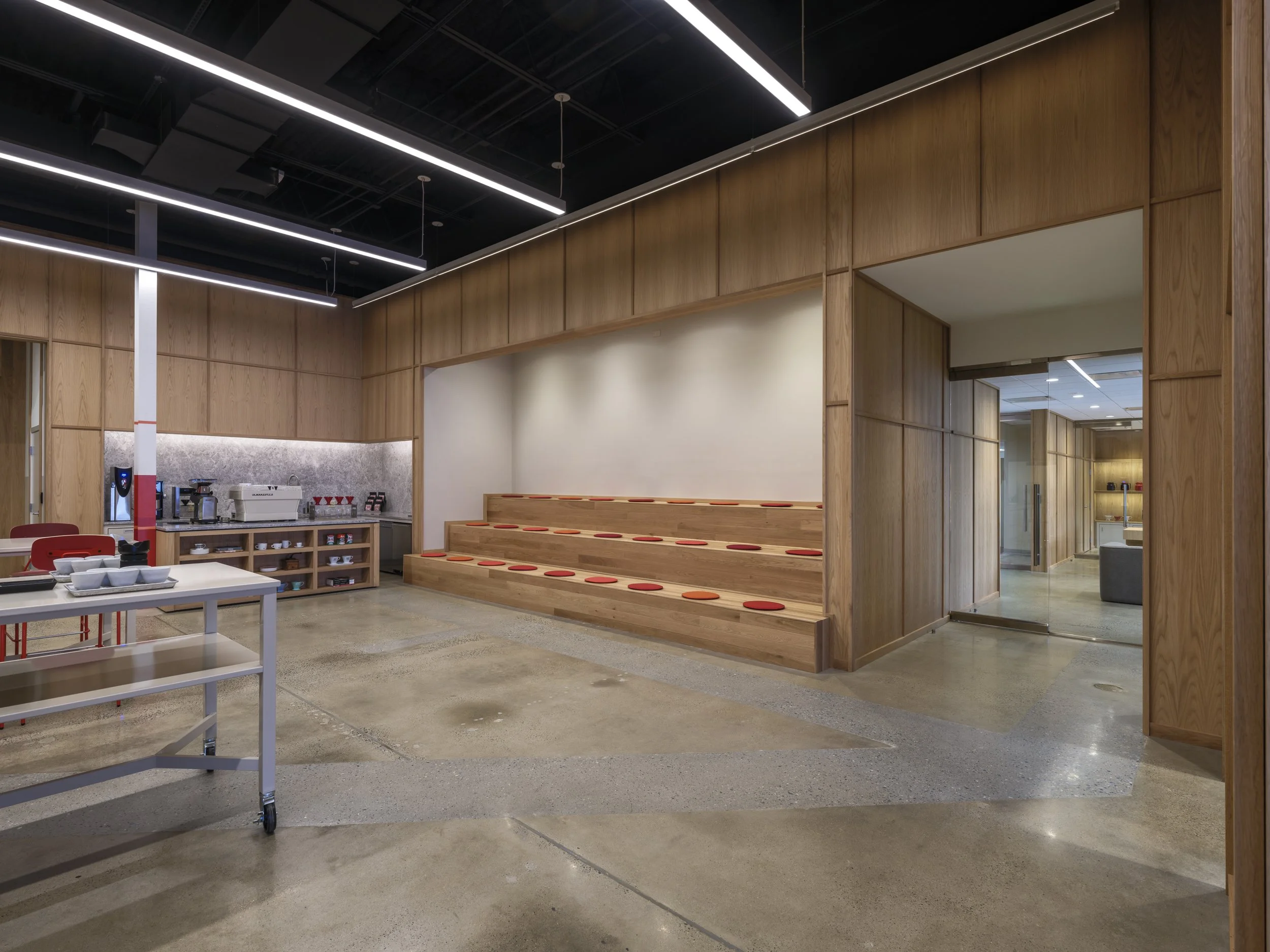 Modern interior space with wooden walls and ceiling, polished concrete floor, and seating area with padded steps and orange cushions.