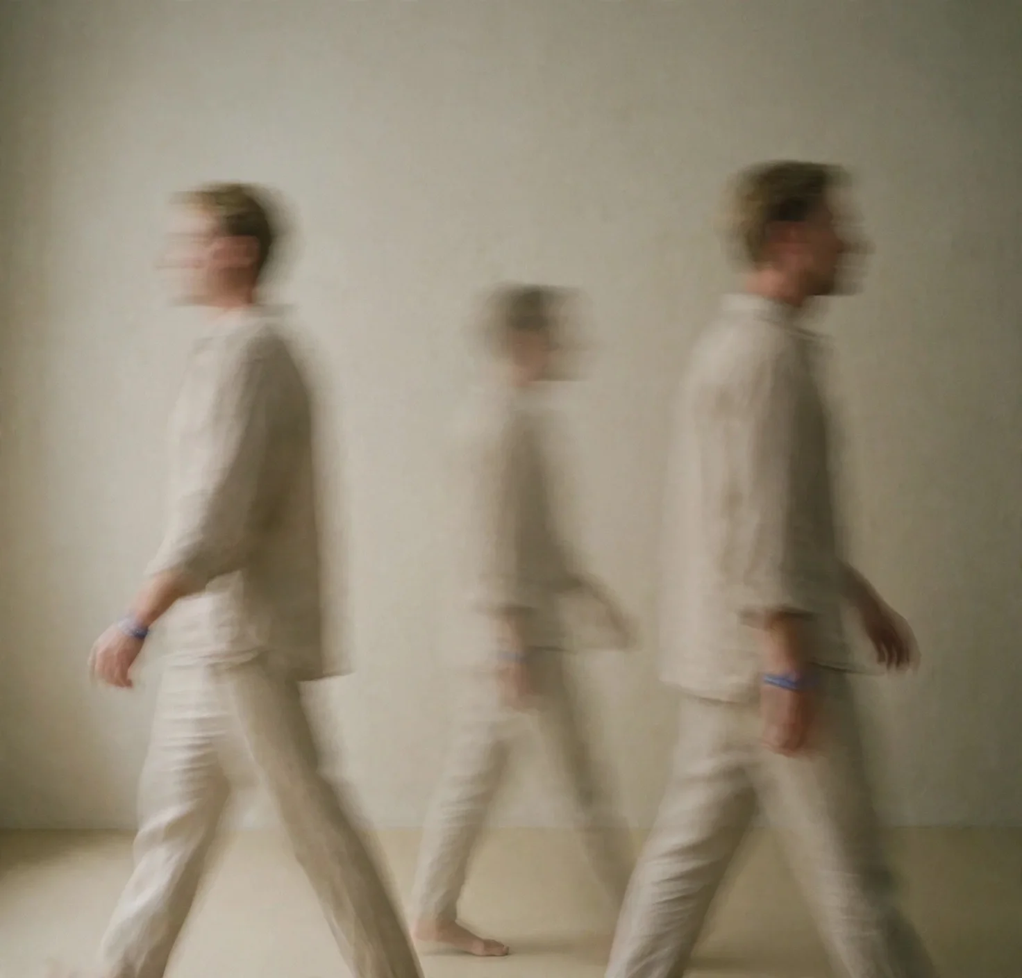 Three people walking in a line, blurred to create a motion effect, against a plain beige wall.