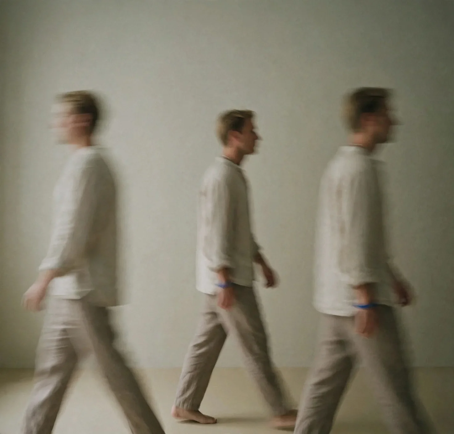 Three young men wearing light-colored clothing walking in a line against a plain background, with motion blur suggesting movement.