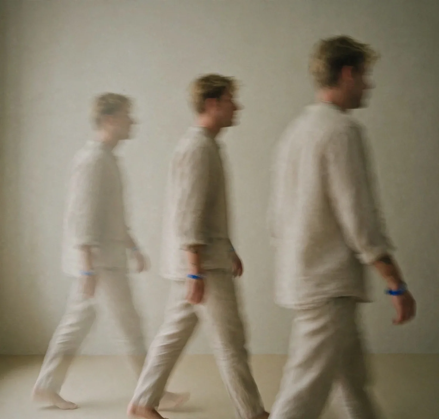 A person walking in front of a neutral background, creating a motion blur effect that shows multiple transparent images of the person in a walking sequence.