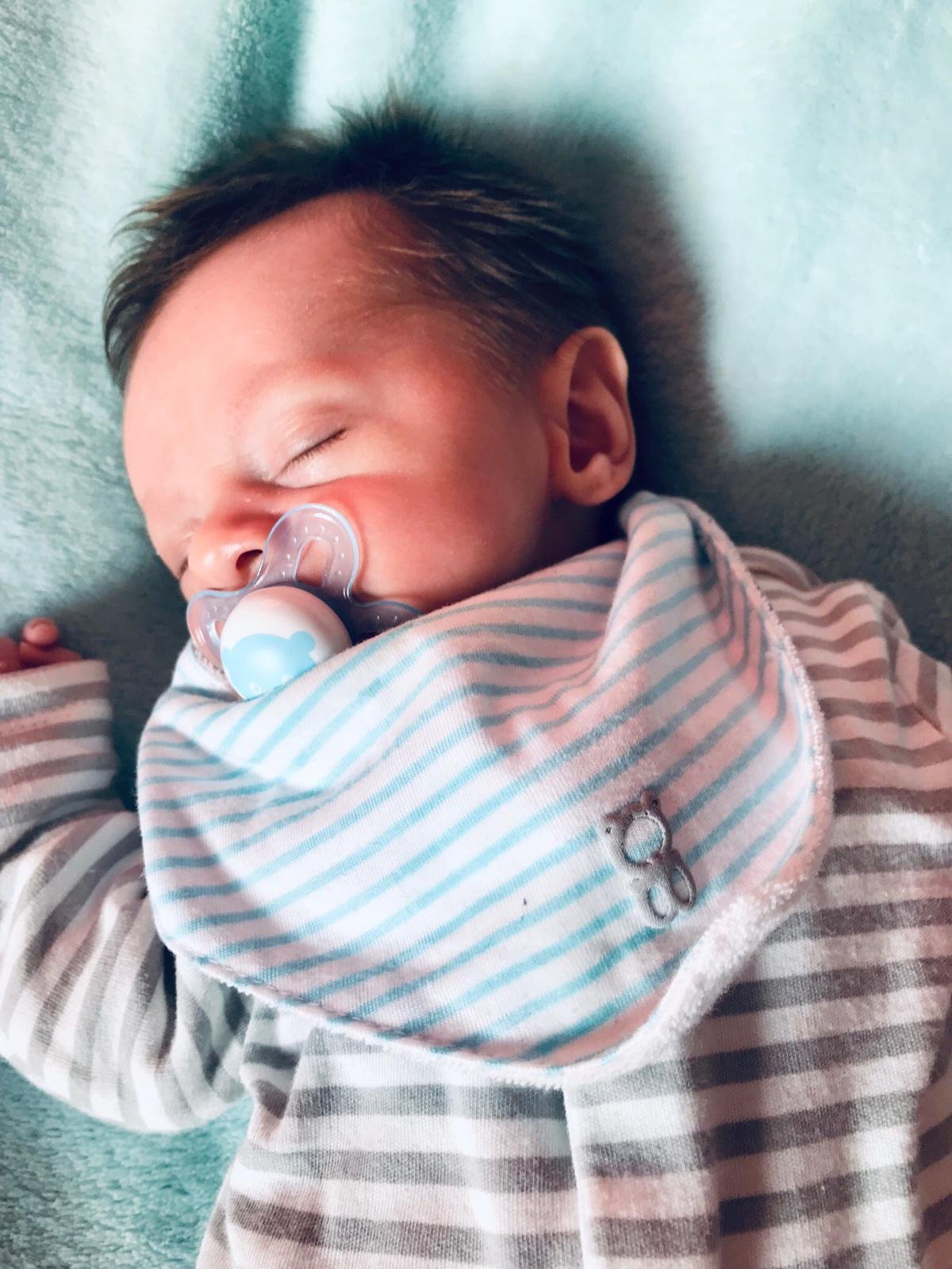 Neonato che dorme con il ciuccio, avvolto in una coperta a righe, in posizione supina su una superficie morbida.