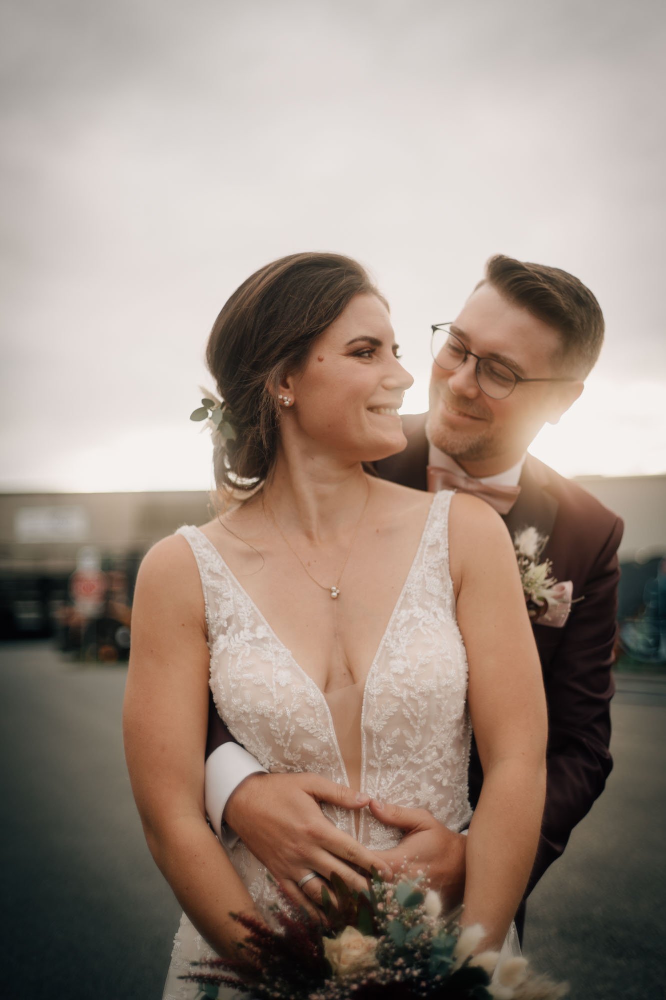 Ein Brautpaar bei der Hochzeit, lachend und verliebt, die Braut trägt ein weißes Hochzeitskleid, der Bräutigam trägt einen Anzug mit Brille.