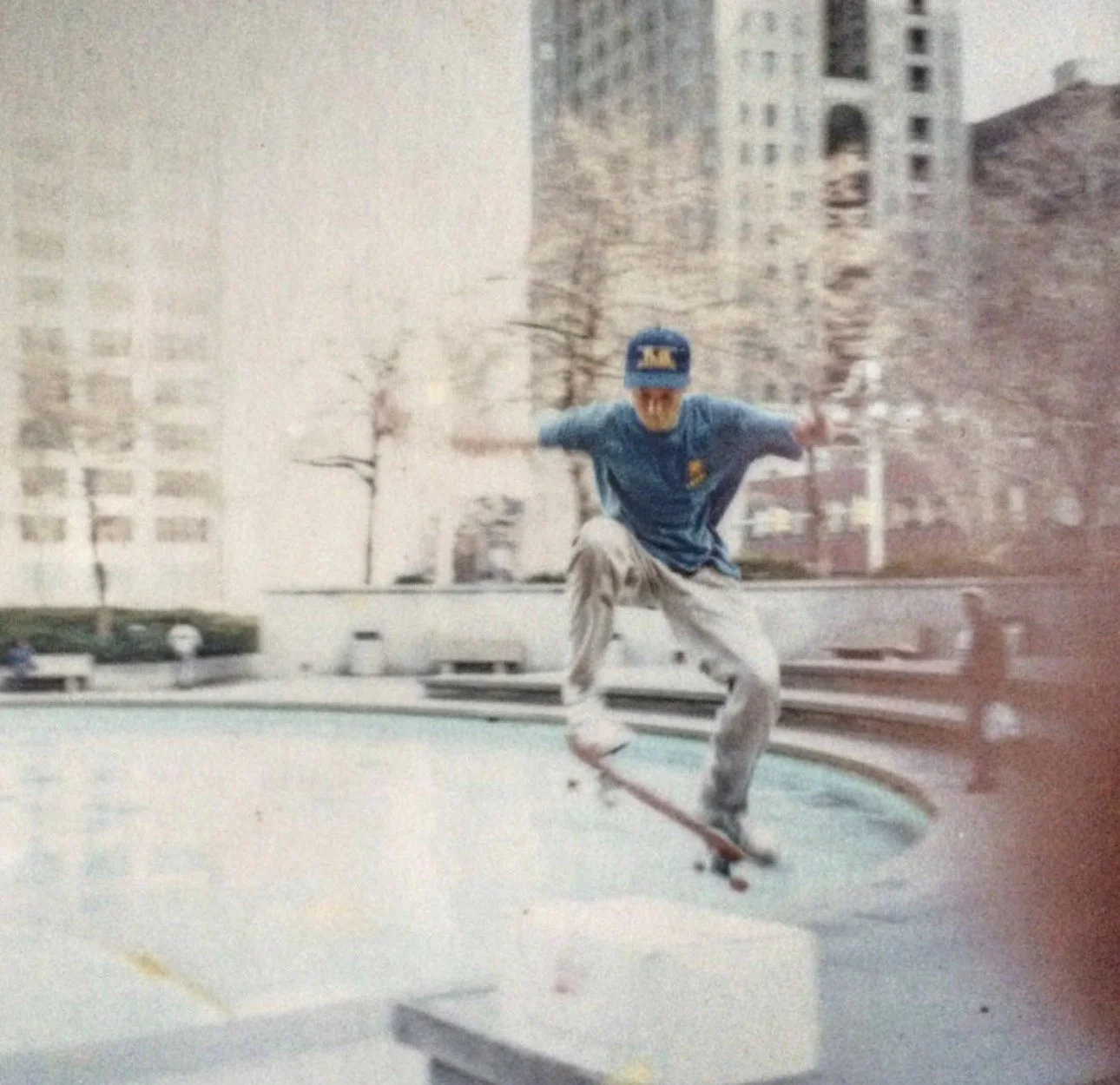 A person skateboarding at a skatepark with city buildings in the background on a cloudy day.