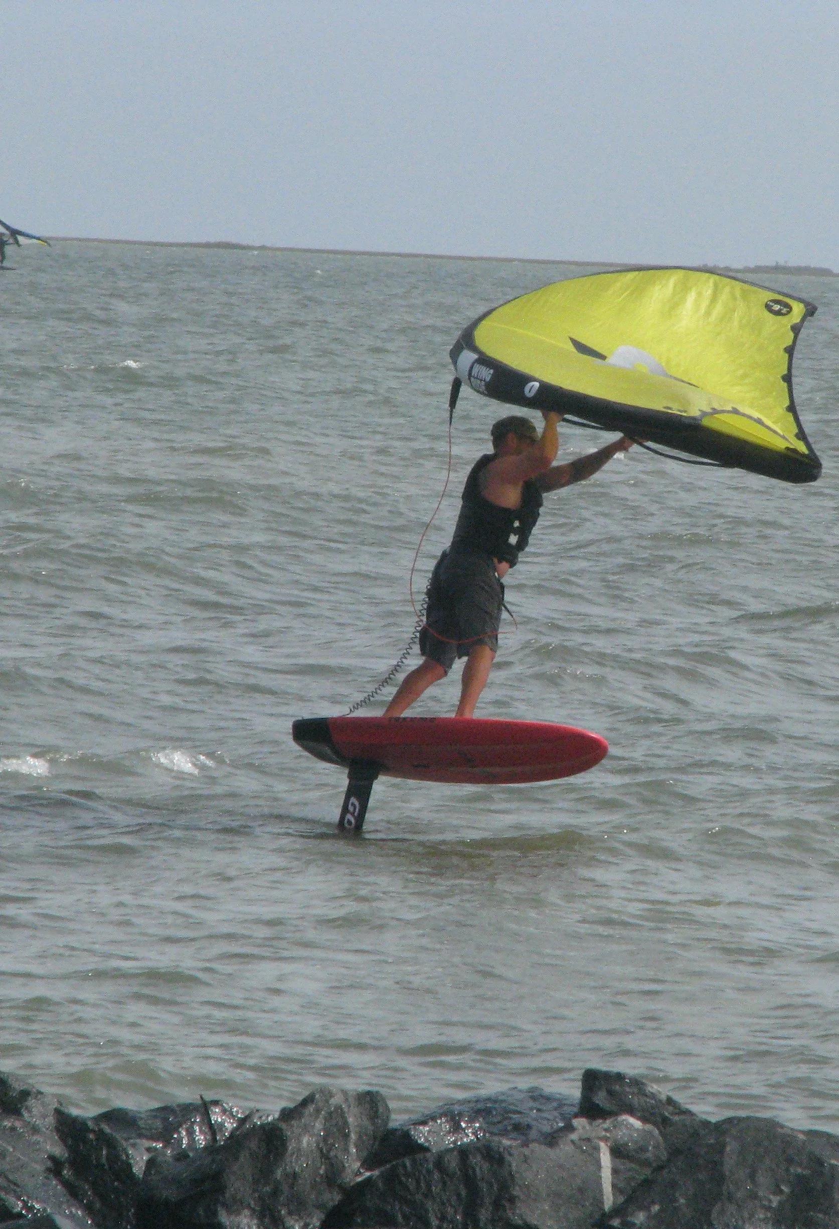 A person riding a hydro foil with a wing foil at the beach. with a cloudy sky in the background.