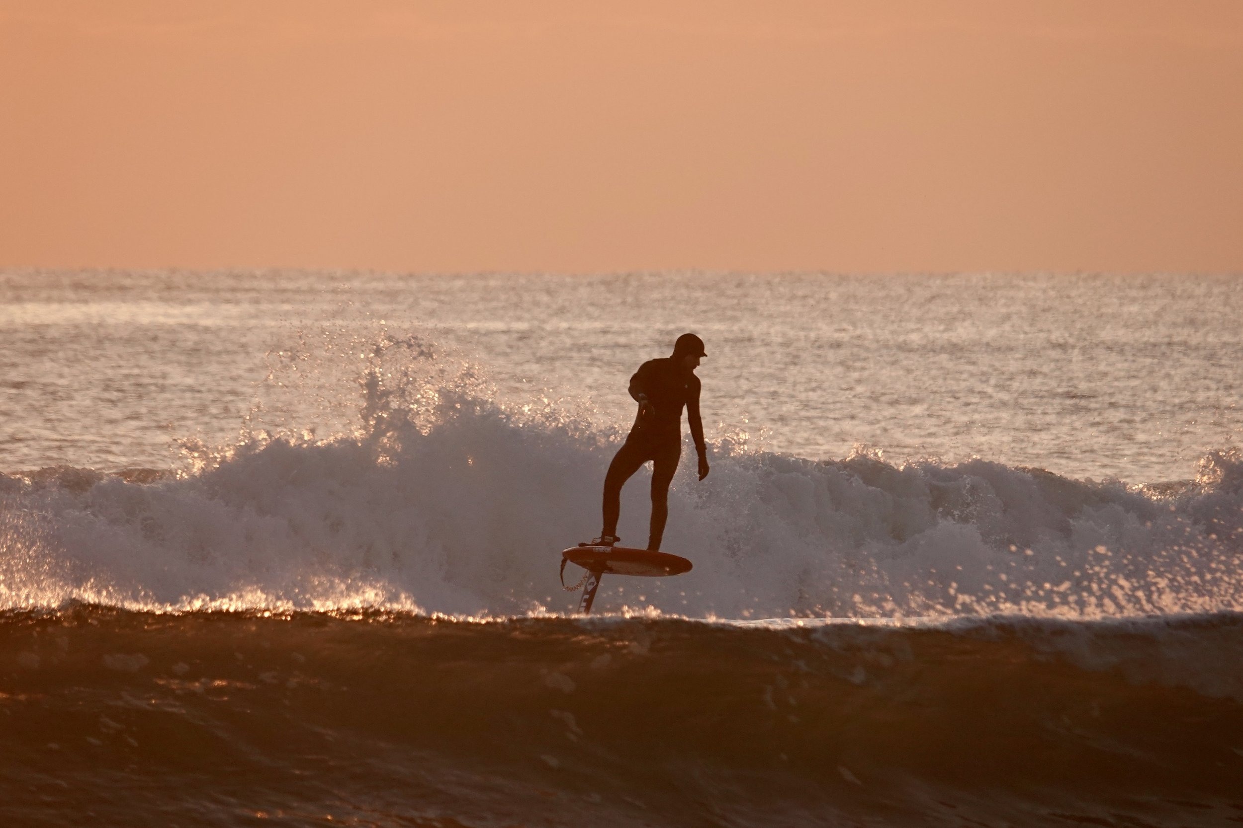 A person surfing on a wave in the ocean during sunset.
