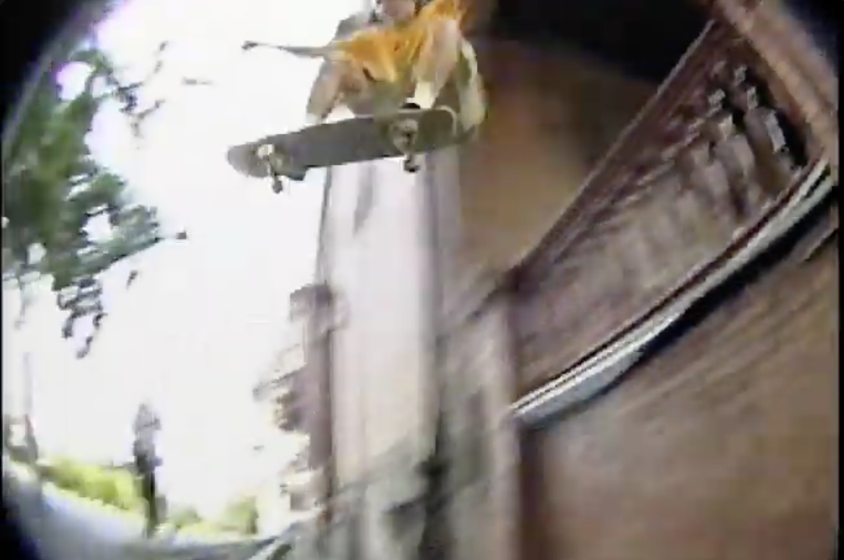 Close-up of skateboard with a yellow object on top, on a wooden surface, with trees and sky in the background.