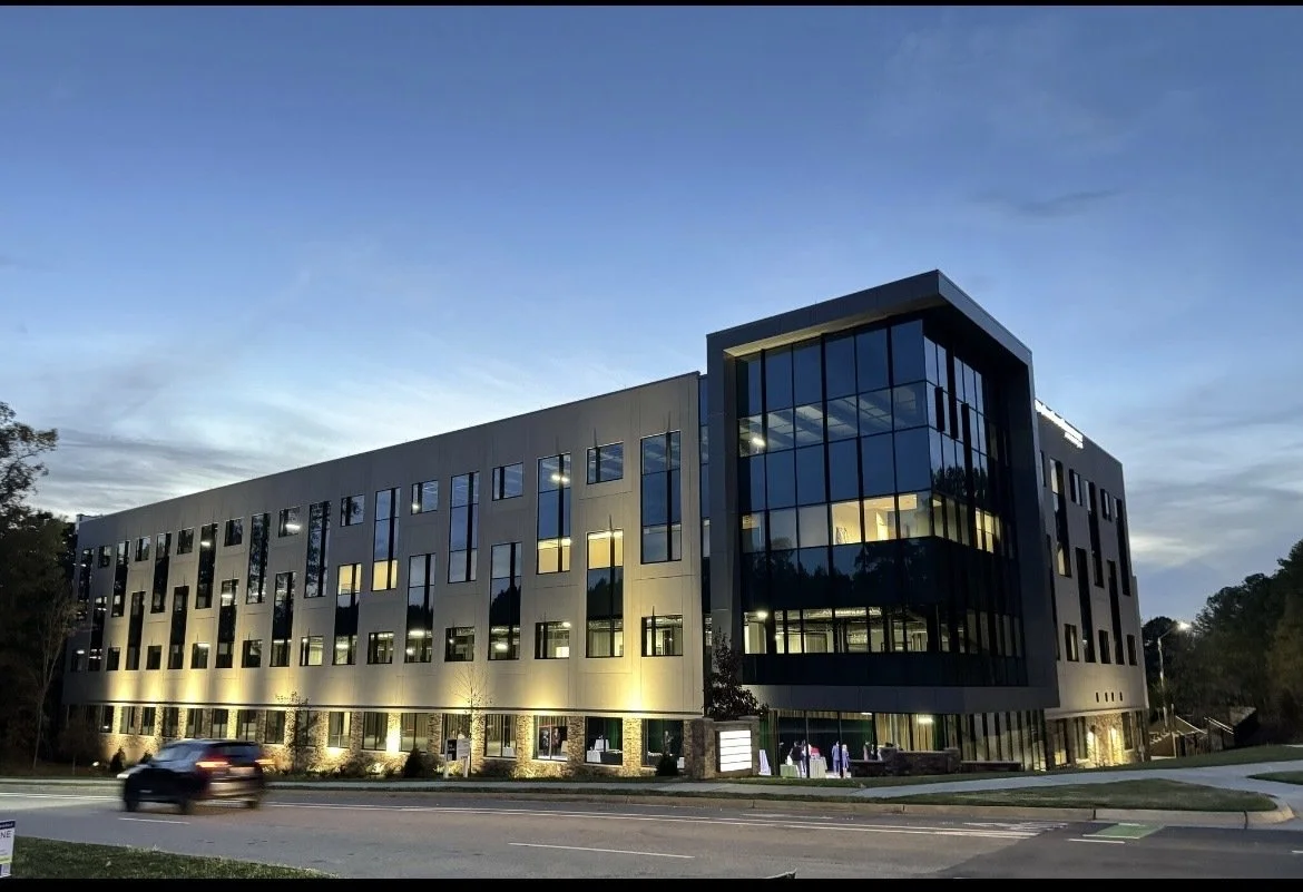 Modern multi-story office building with large glass windows illuminated at dusk.