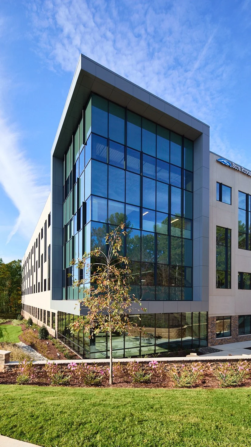 Modern glass office building with landscaped garden and blue sky.