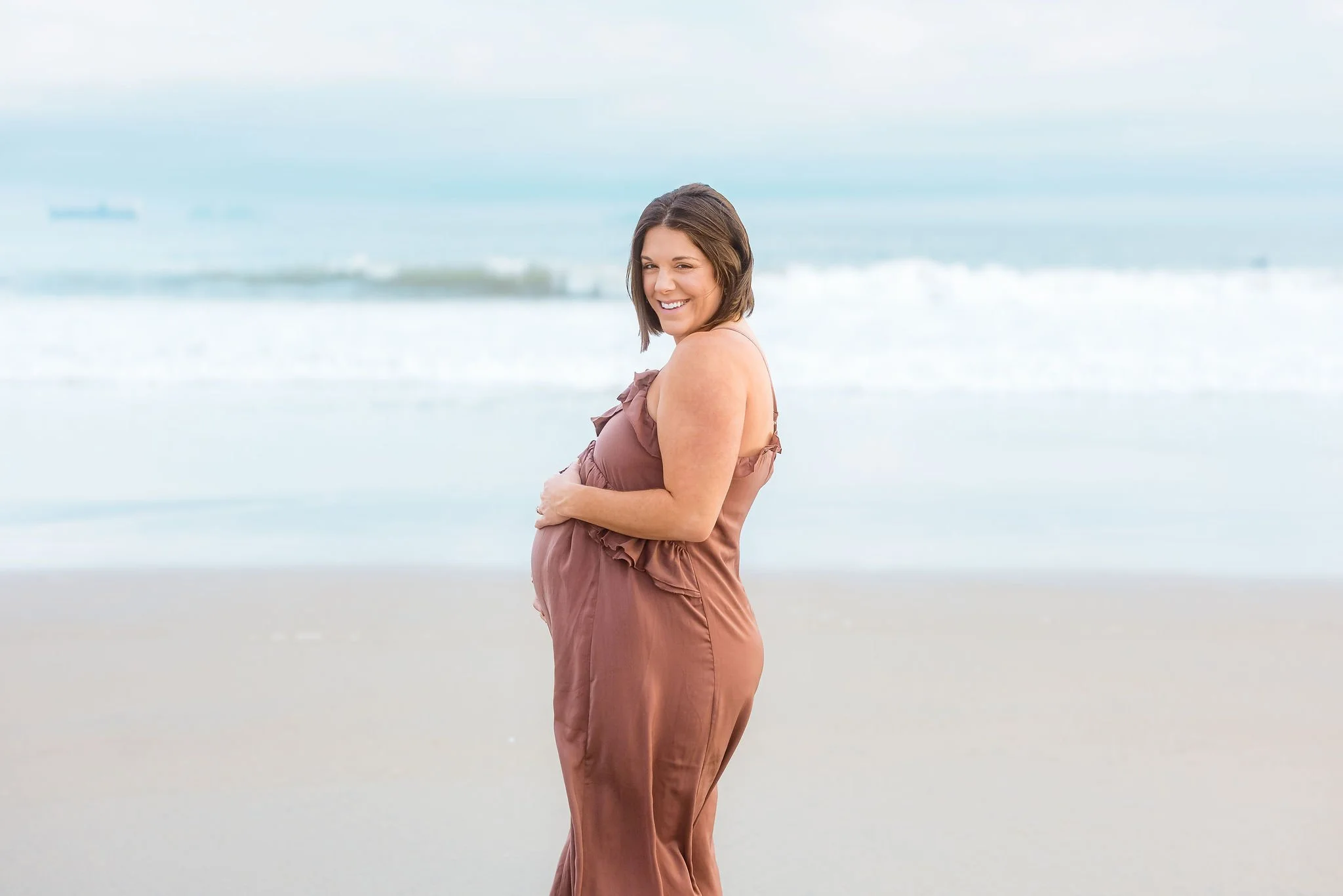 AnnMarie Rose, business strategist, taking maternity photos on a beach with the ocean in the background