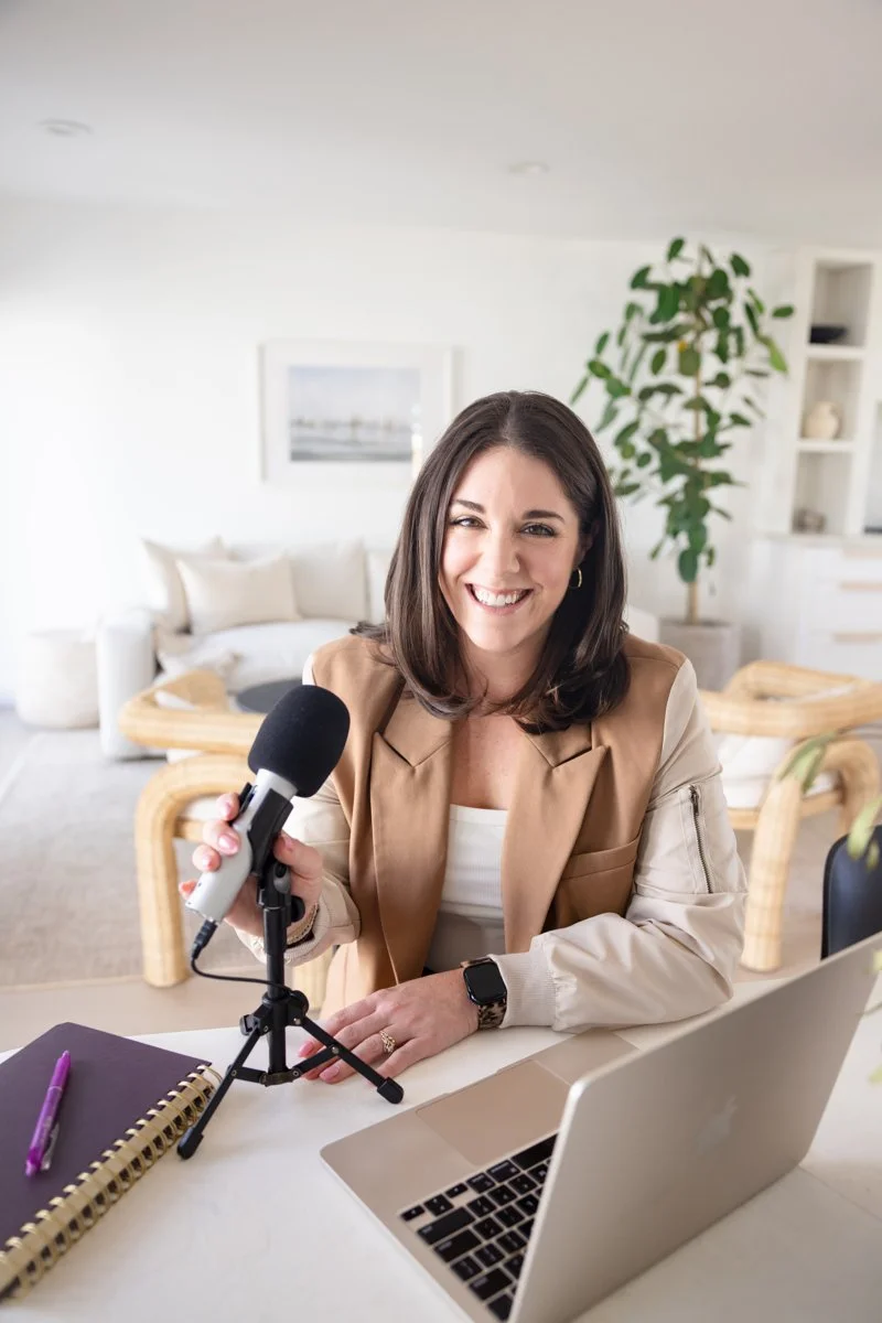 Business strategist sitting down smiling with a microphone, notebook, and macbook