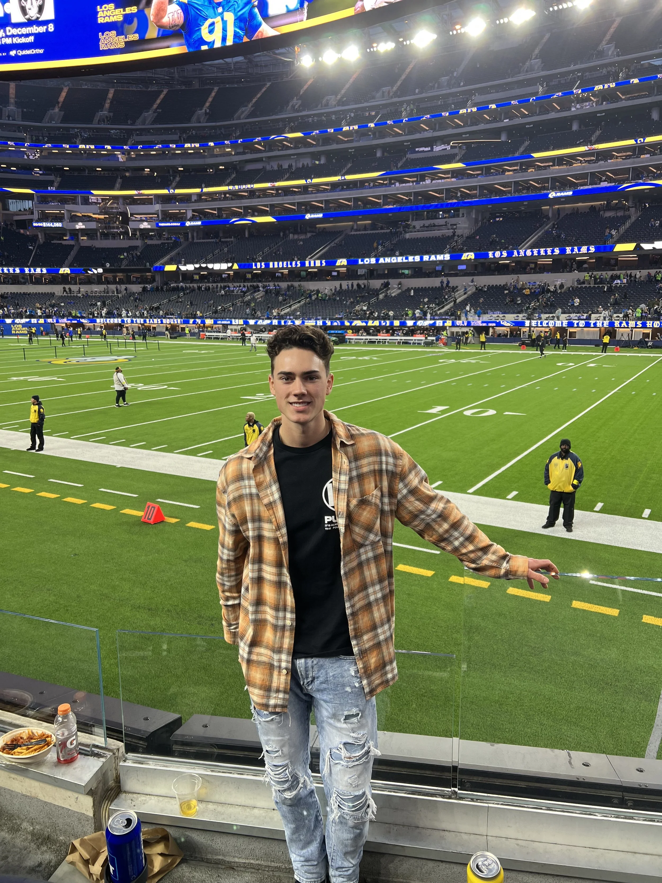 A young man, the founder, standing at the edge of a football field inside a stadium, smiling at the camera, taking in the moment after the game.