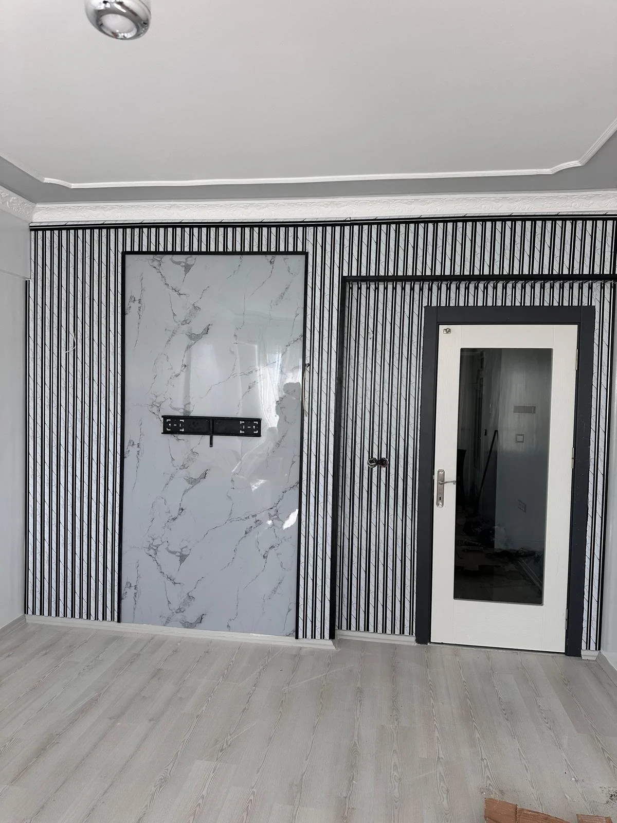 Odanın duvarlarındaki dekoratif tasarım, biri mermer desenli duvar paneli diğerleri çizgili desenli modern duvarlar ve içeriği görülmeyen kapı.