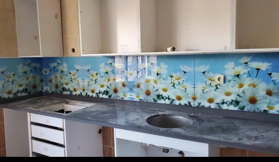 Mutfak tezgahında cam arkasında papatya çiçekleri desenli sıva. Aynada yansıyan camın dışarıdan görünüşü ve birkaç elektrik prizi bulunmaktadır.