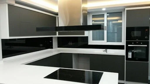 Modern bir mutfak, siyah ve beyaz renklerde, elektrikli ocak ve mikrodalga içeren dolaplar ve tezgahlar ile donatılmış.