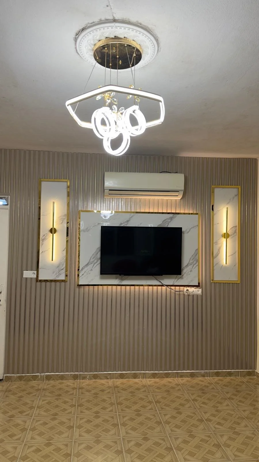 Modern oturma odası duvarı ve asılı televizyon, parlak beyaz ve altın detaylı aynalar, ve LED aydınlatmalı modern avize.