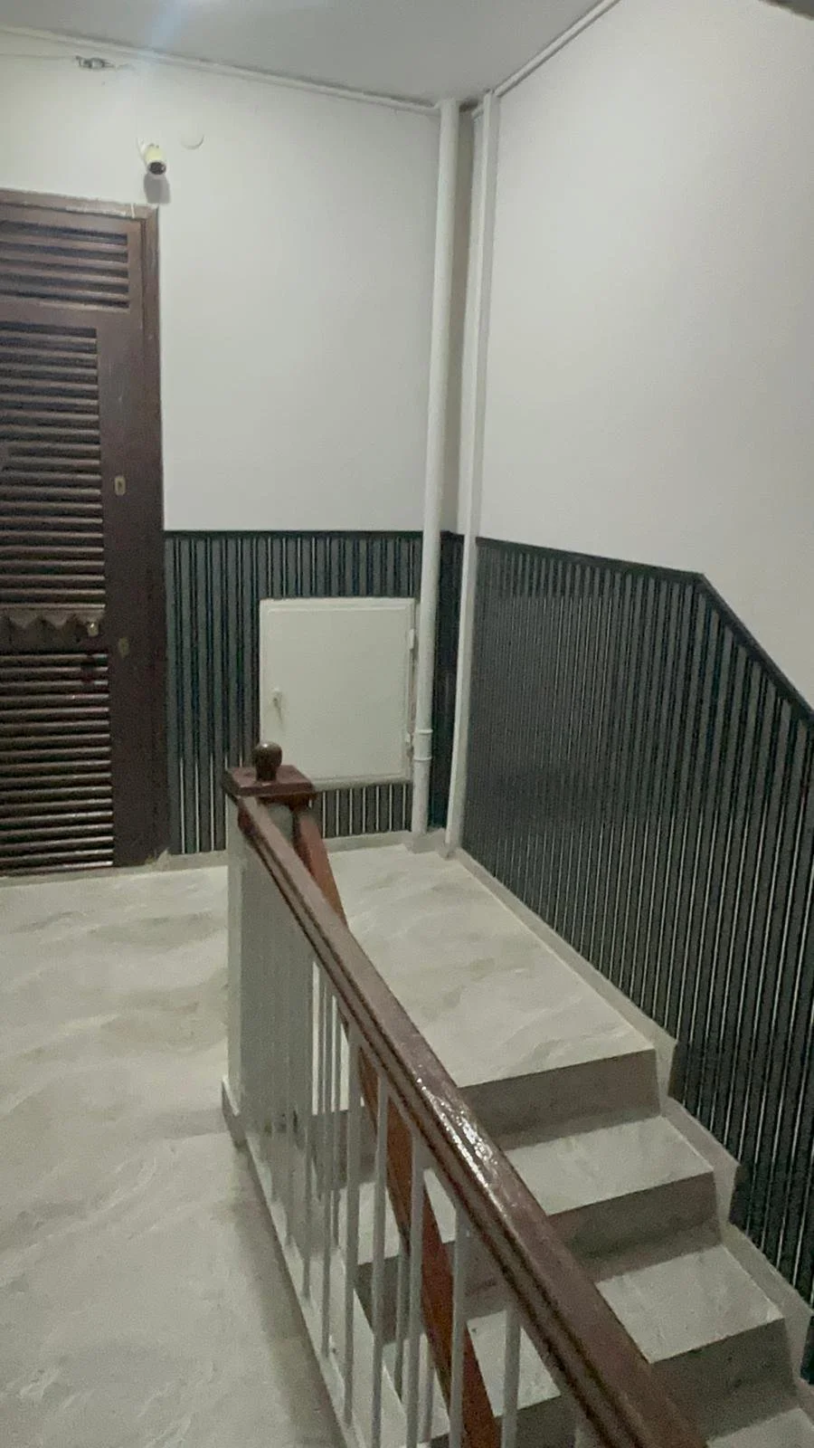 İç mekanda birkaç basamaktan oluşan merdivenler ve ahşap korkuluk. Duvarlarda siyah ve beyaz renklerin kullanıldığı odanın köşesinde bir kapı ve duvarlarda bir kutu ve borular var.