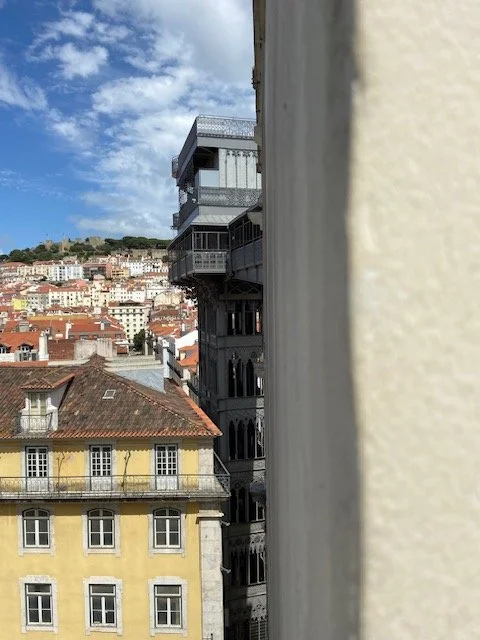 Cityscape view through a narrow gap with buildings, including the historic Santa Justa Lift in Lisbon, Portugal.