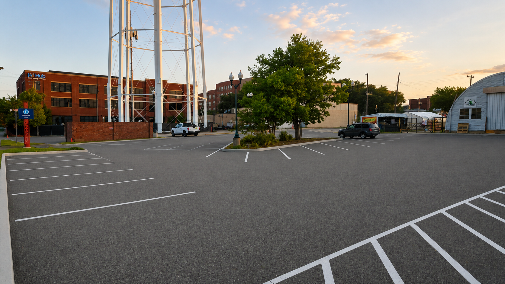 Empty parking lot with a few cars, trees, and buildings in the background at sunset.