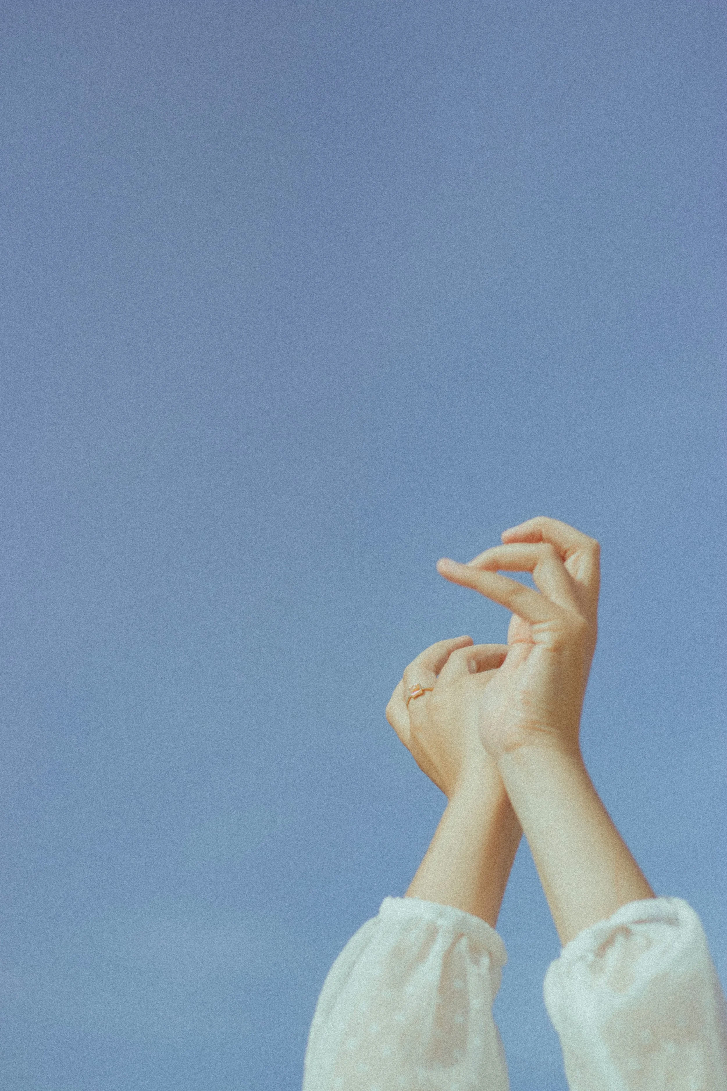 Close-up of a person's hands with rings, posed against a blue sky, with the person's sleeves rolled up.