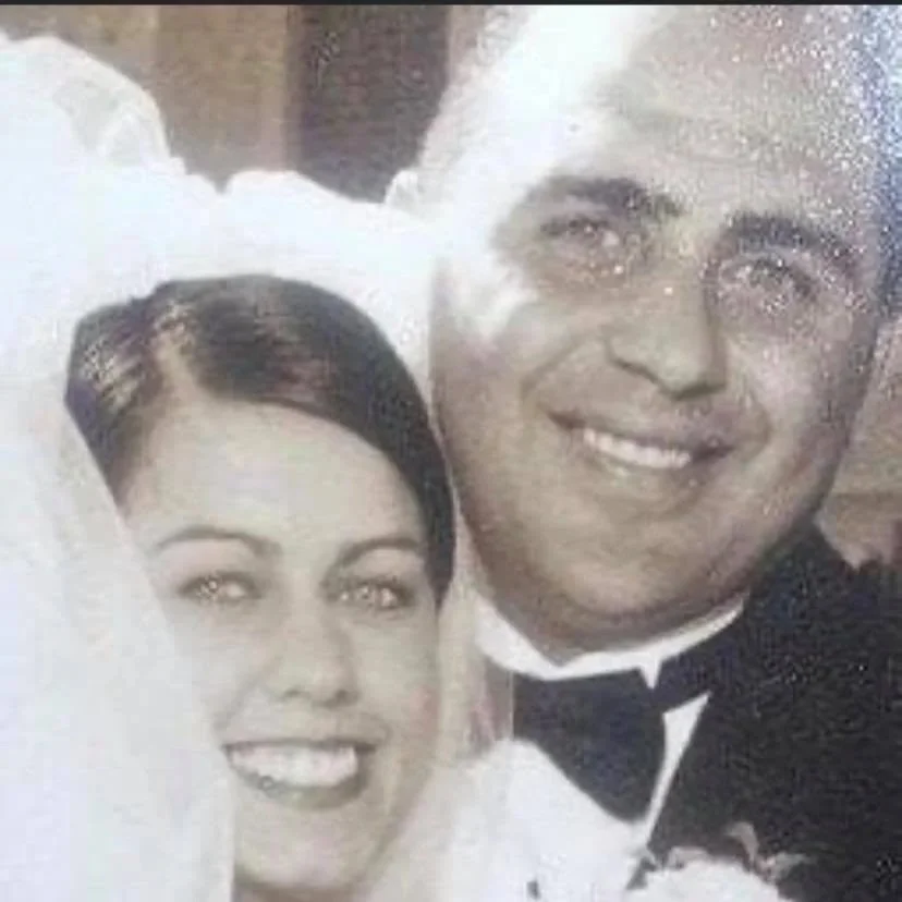 A black-and-white photo of a smiling bride and groom in wedding attire, close together, with a misty or foggy effect partially obscuring the image.