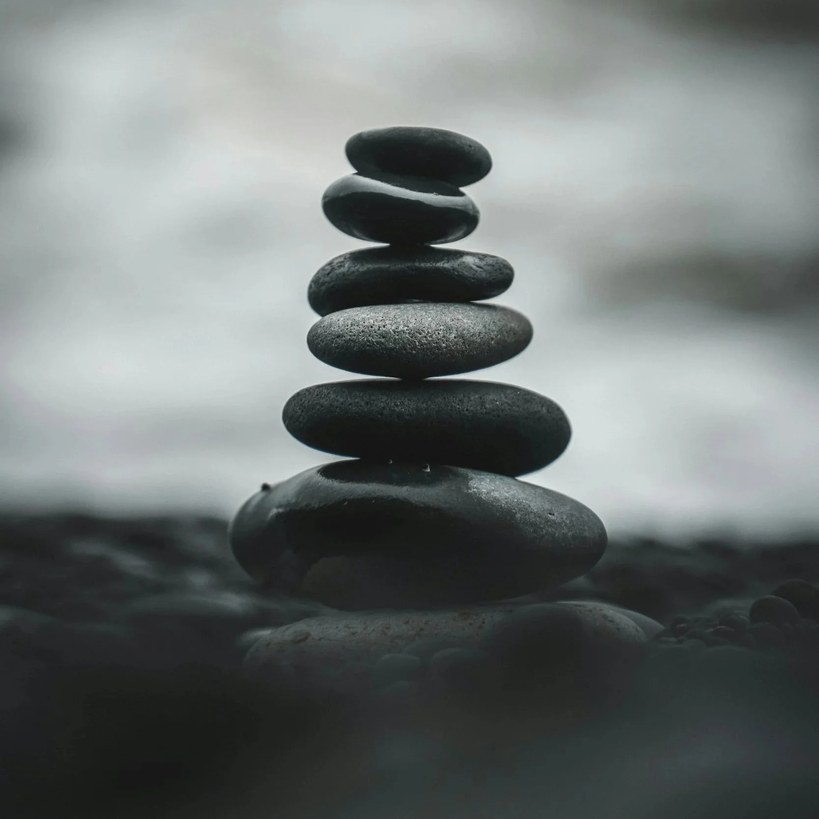 Stacked smooth black stones on water surface with blurred background.