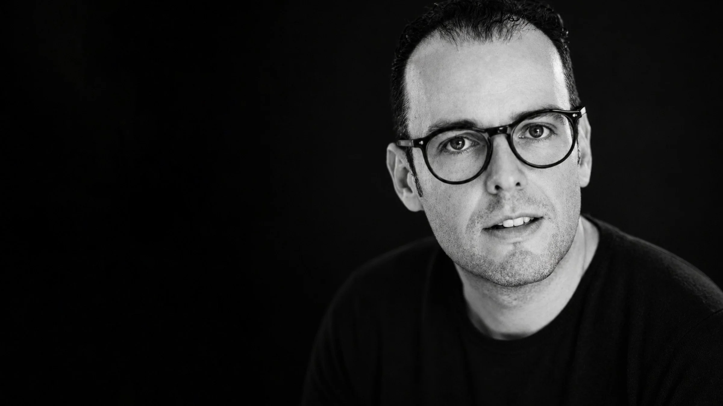 Portrait of Mexican contemporary artist Fer Quirarte smiling at the camera against a dark background.