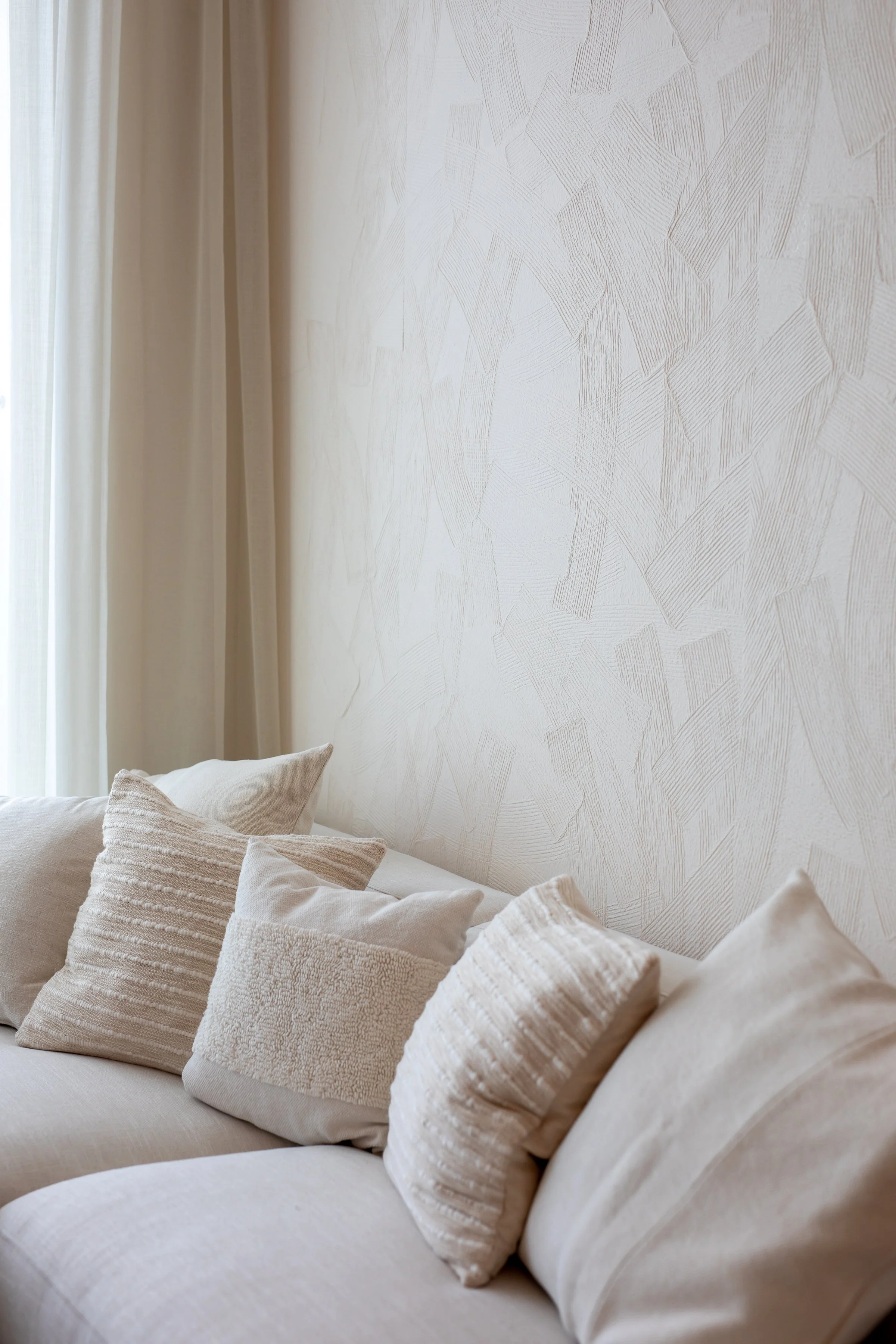 A serene living room interior by Trace Design Studio featuring a cream linen sofa, textured washi wallpaper, and sheer linen curtains — residential interior design Miami.