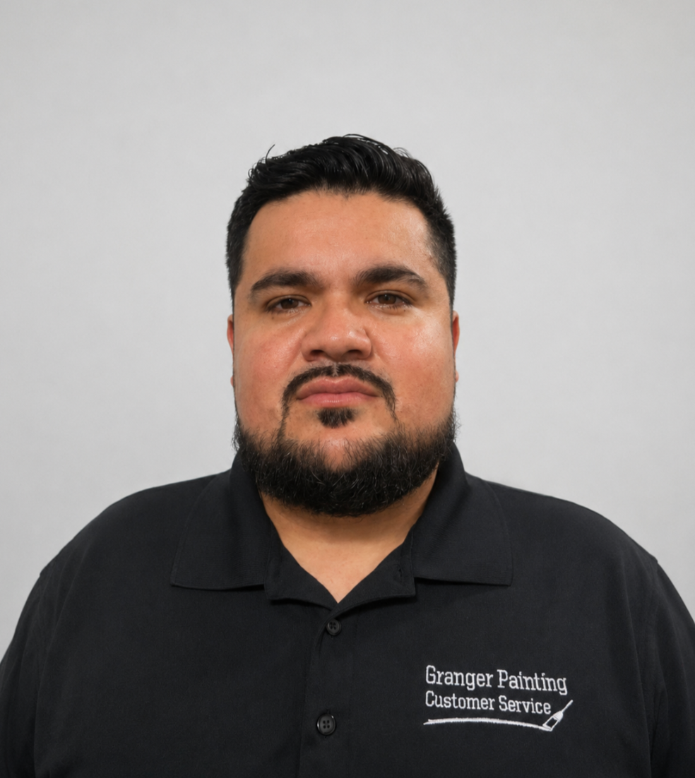 A man with dark hair and a beard, wearing a black polo shirt with the words "Granger Painting Customer Service" embroidered on it, standing against a plain light grey background.