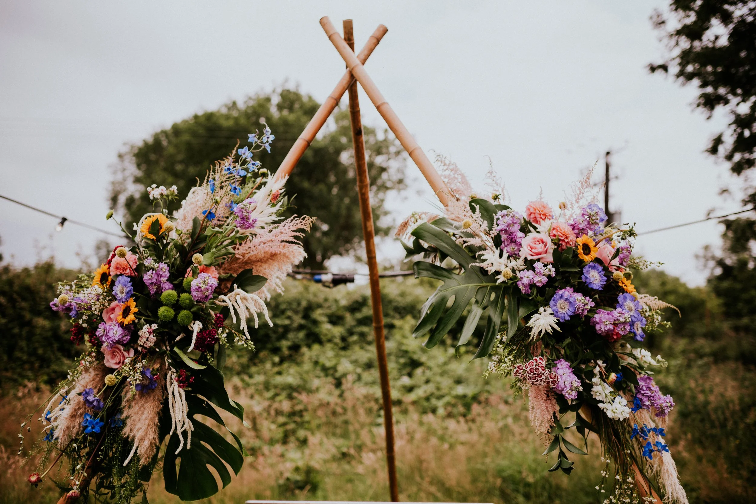 Colorful flower arrangement on a stand, with pink, purple, yellow, blue, and white flowers, set outdoors during daytime.