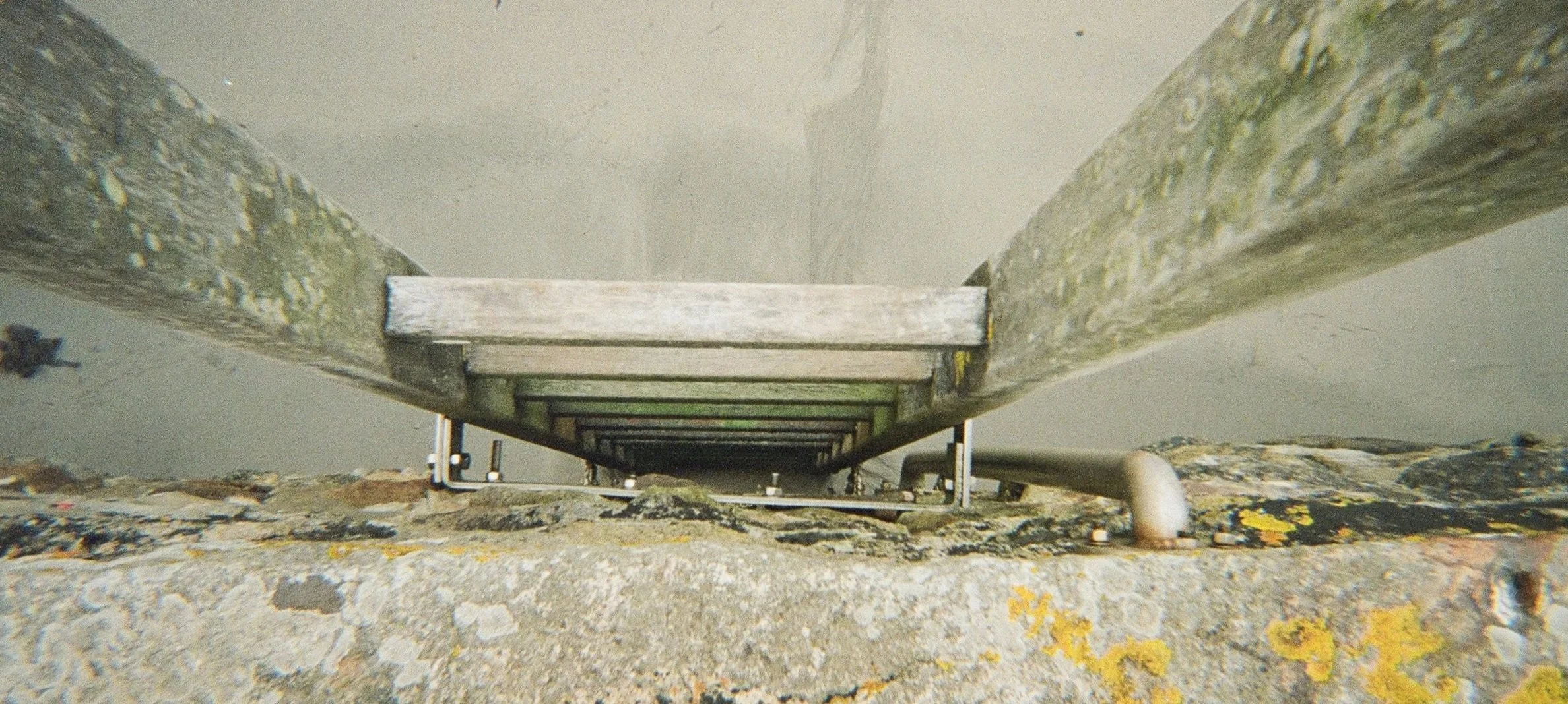 Looking down a ladder from the top, showing wooden and metal parts, with trees and rocky ground below.