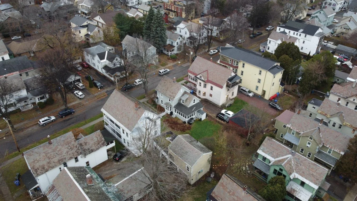 An aerial view of a residential neighborhood with various houses, trees, and parked cars on the streets and driveways.