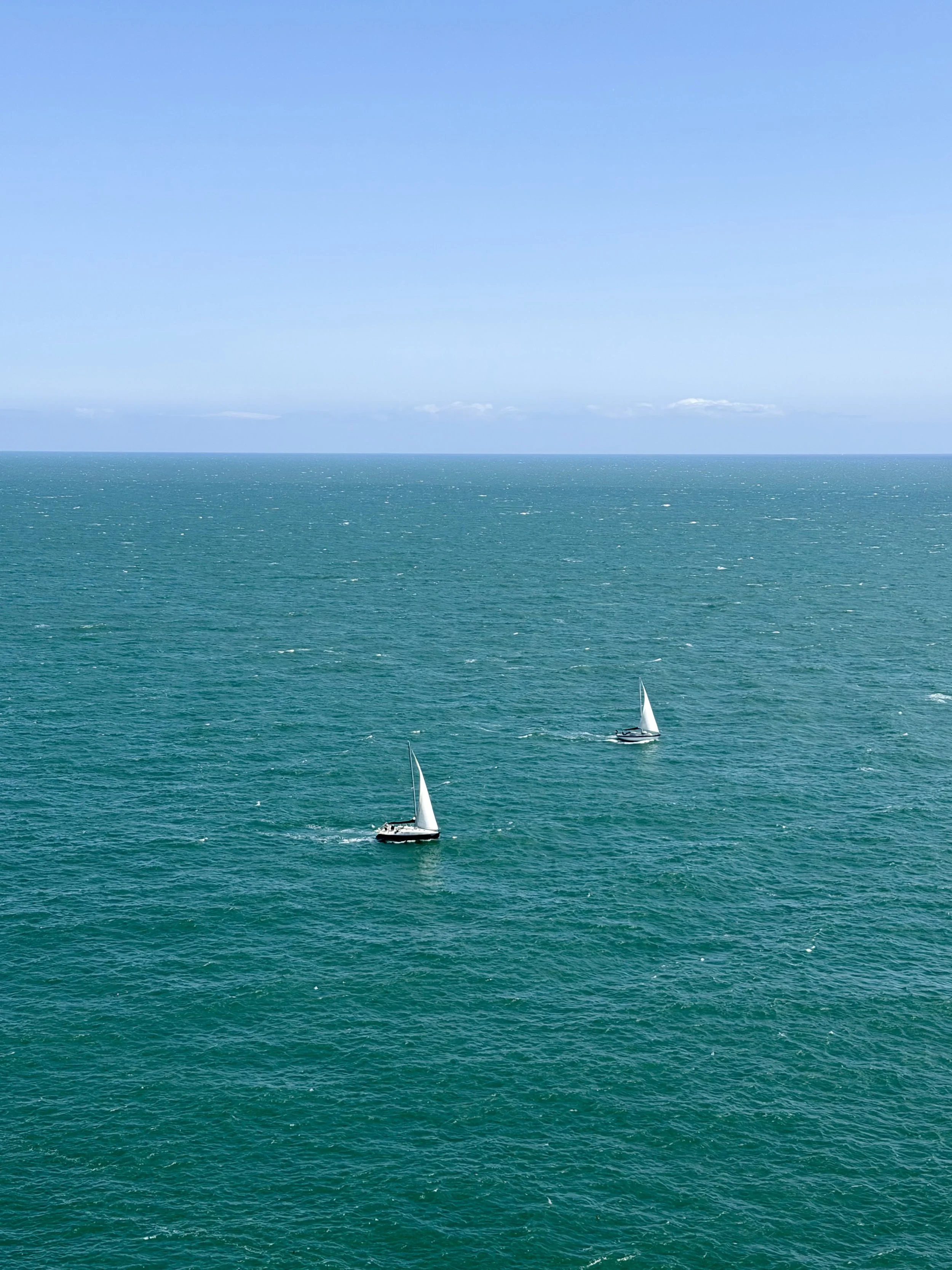 Two sailboats sailing on calm blue ocean under a clear sky.