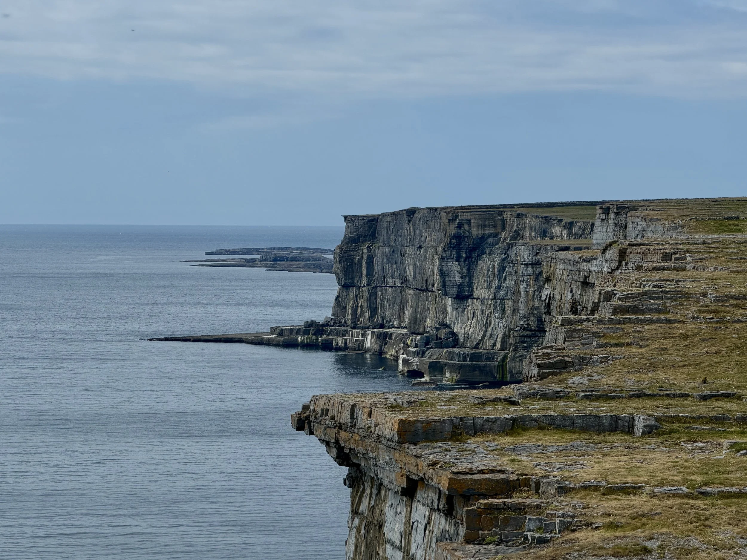 Cliffs along a rocky shoreline with the sea below and a cloudy sky above.