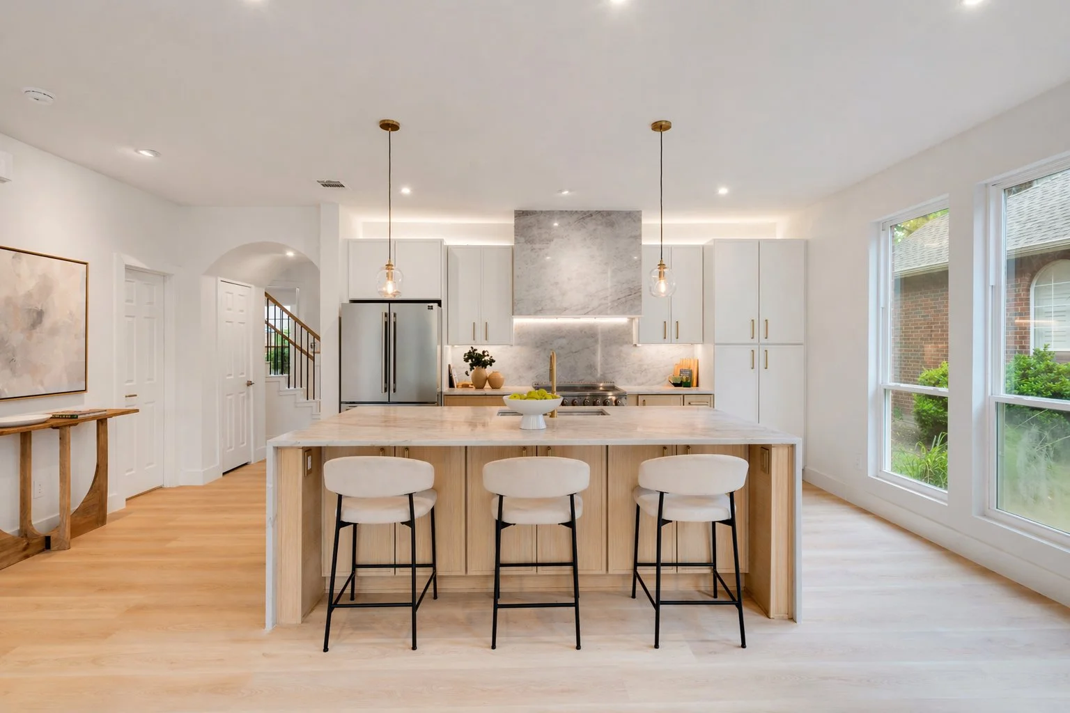 Bright modern kitchen with white cabinetry, marble backsplash, and a large island with three white barstools.